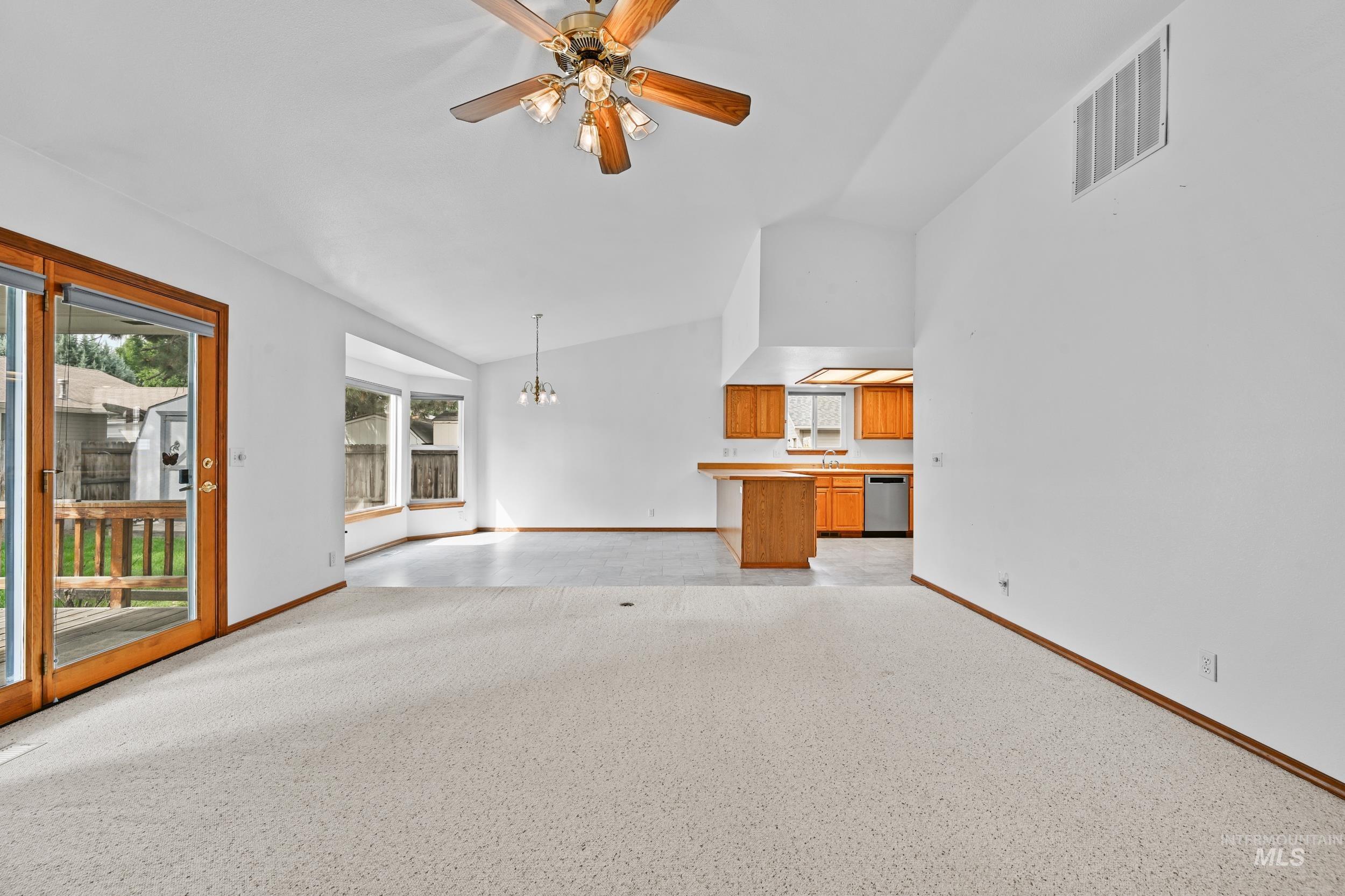 Unfurnished living room with lofted ceiling, a ceiling fan, and a chandelier