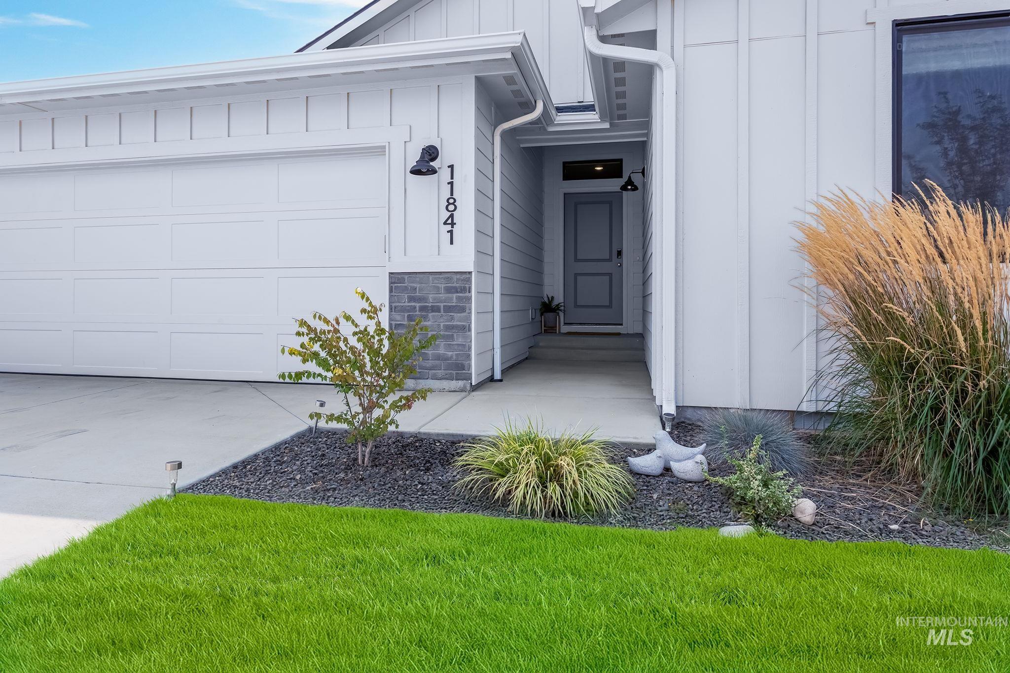 View of exterior entry featuring board and batten siding, stone siding, driveway, and an attached garage