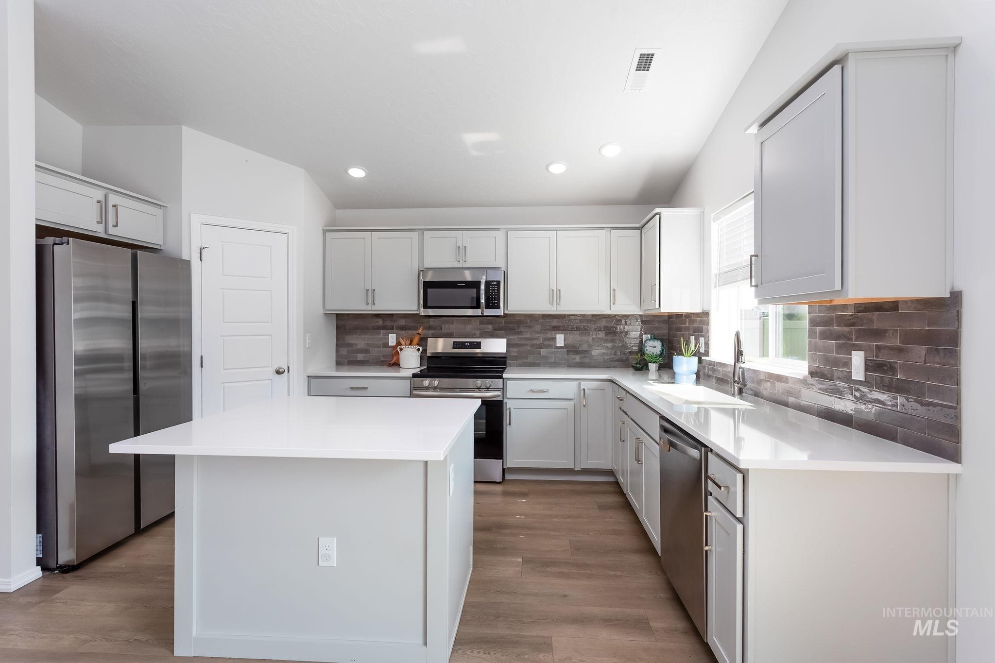 Kitchen featuring stainless steel appliances, a kitchen island, backsplash, recessed lighting, and light wood-style flooring
