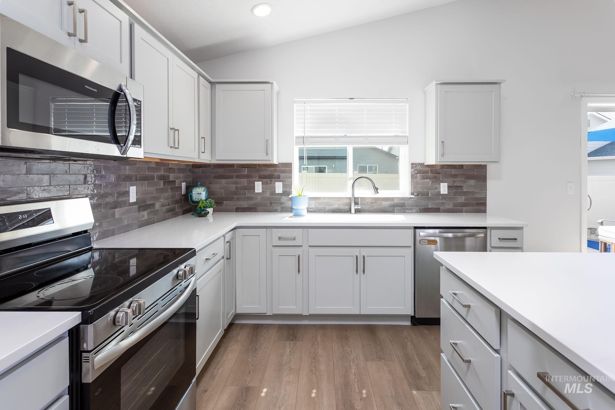 Kitchen featuring appliances with stainless steel finishes, light wood finished floors, decorative backsplash, vaulted ceiling, and white cabinetry