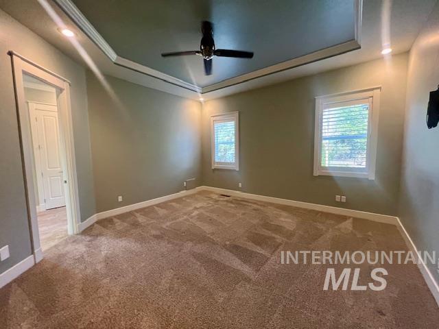 Empty room with a tray ceiling, carpet flooring, a ceiling fan, and crown molding