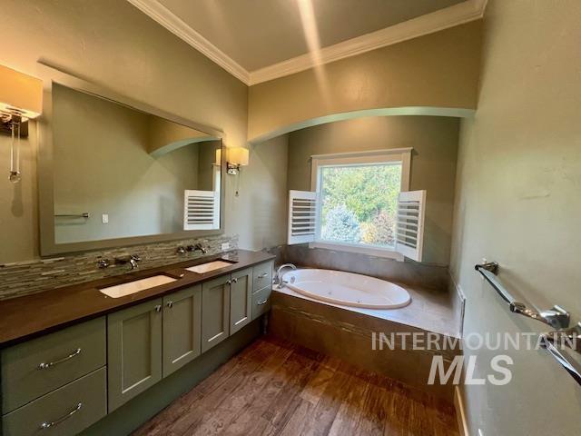 Full bathroom with double vanity, ornamental molding, a bath, dark wood finished floors, and tasteful backsplash