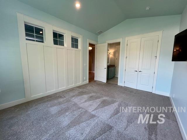 Unfurnished bedroom with ensuite bathroom, vaulted ceiling, and carpet flooring