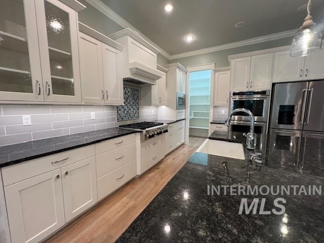Kitchen featuring dark stone countertops, white cabinetry, appliances with stainless steel finishes, backsplash, and ornamental molding