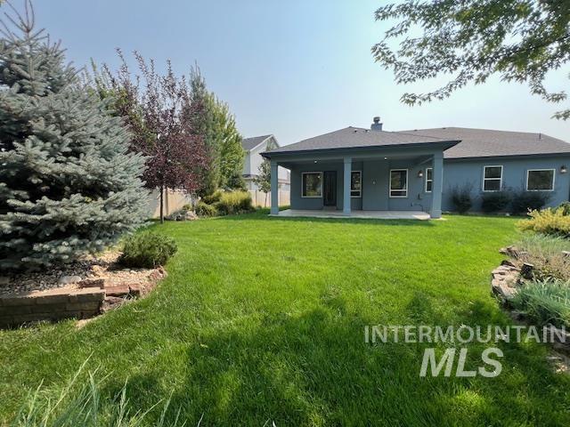 Back of house featuring a patio, a yard, stucco siding, and a chimney