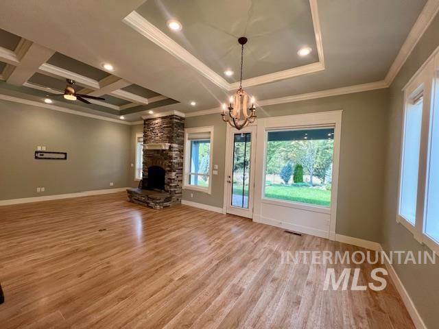 Unfurnished living room featuring ornamental molding, light wood-style floors, a chandelier, a stone fireplace, and a ceiling fan