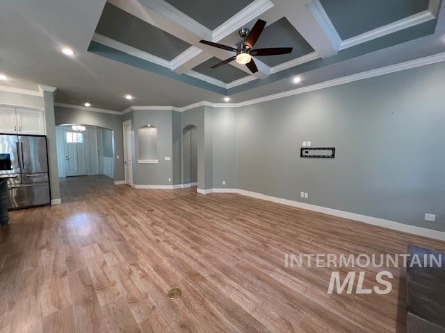 Unfurnished living room with crown molding, arched walkways, coffered ceiling, wood finished floors, and ceiling fan