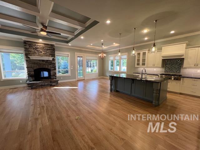 Kitchen featuring white cabinetry, open floor plan, decorative light fixtures, ornamental molding, and glass insert cabinets