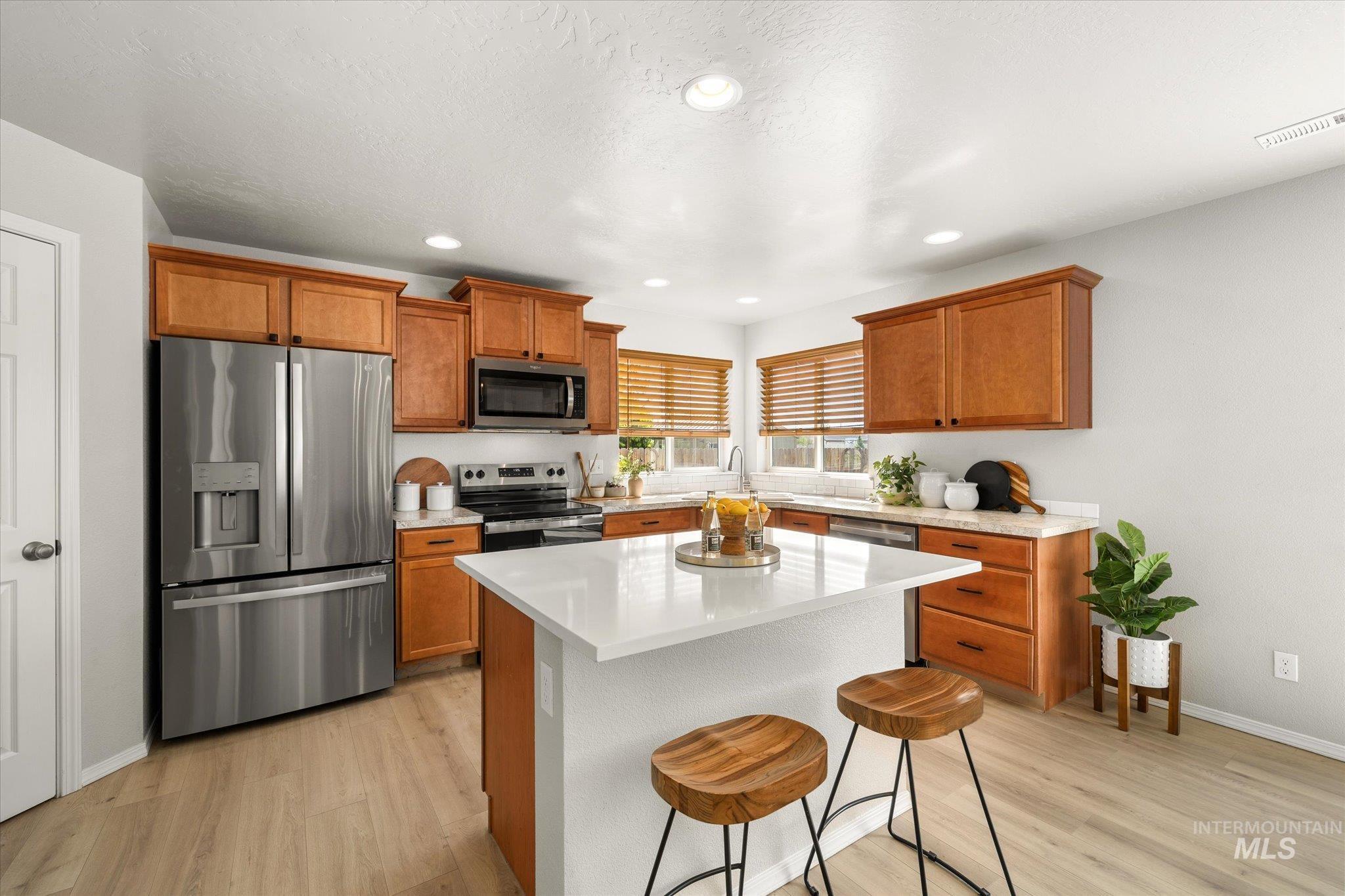 Kitchen featuring appliances with stainless steel finishes, brown cabinetry, a breakfast bar, light wood-style flooring, and recessed lighting
