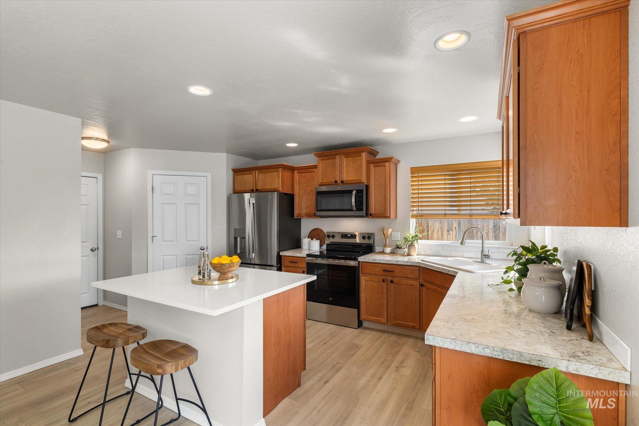 Kitchen featuring a breakfast bar area, appliances with stainless steel finishes, light wood finished floors, brown cabinets, and recessed lighting