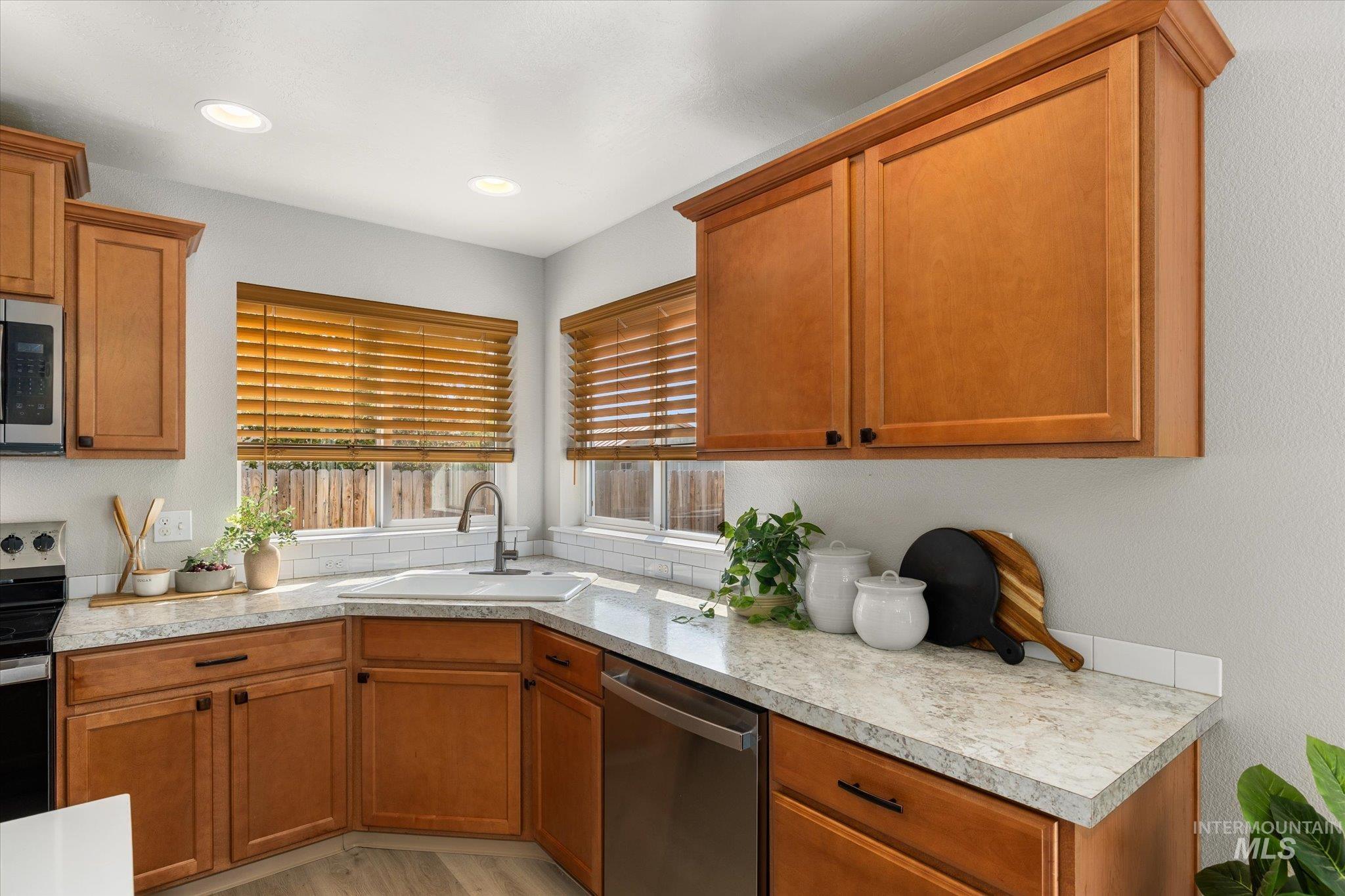 Kitchen with appliances with stainless steel finishes, brown cabinets, light countertops, light wood-type flooring, and recessed lighting