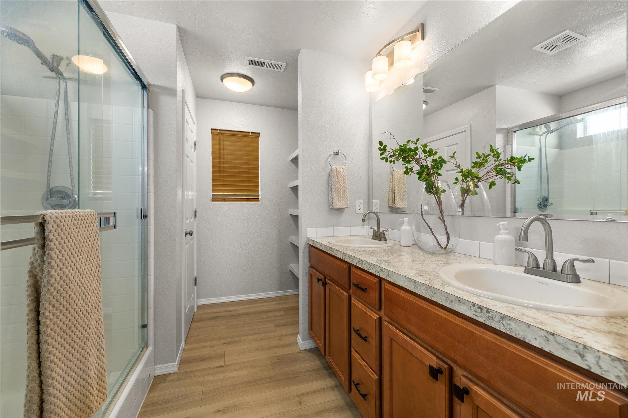 Bathroom featuring a stall shower, double vanity, and light wood-style flooring