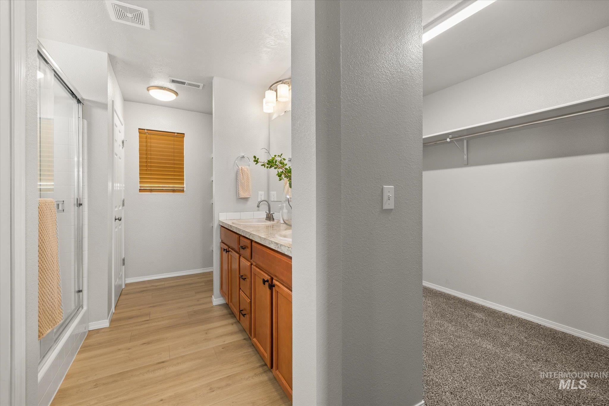 Full bathroom featuring double vanity, a shower stall, light wood-type flooring, and a textured wall