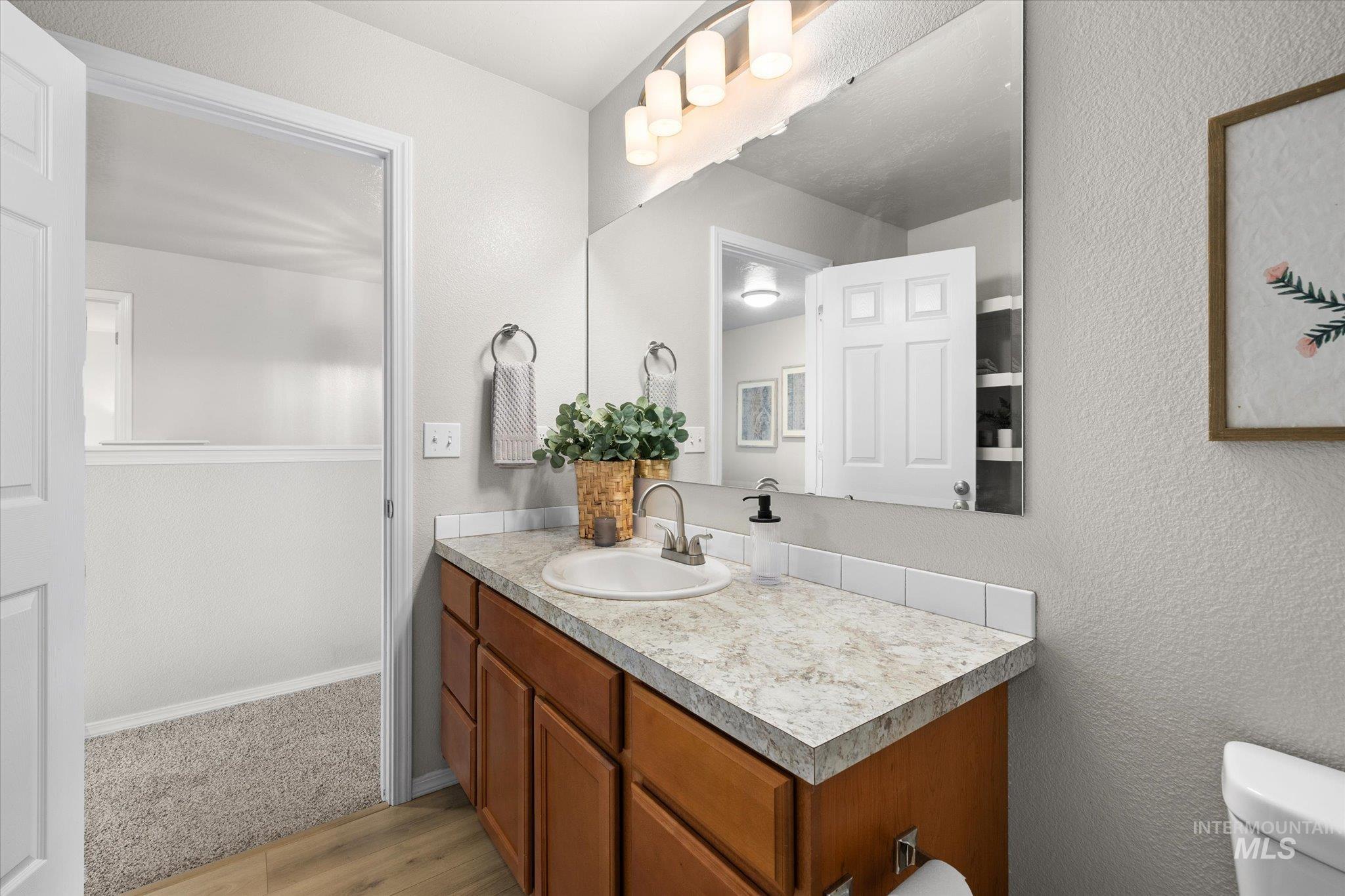 Half bathroom with vanity, a textured wall, and light wood-style floors
