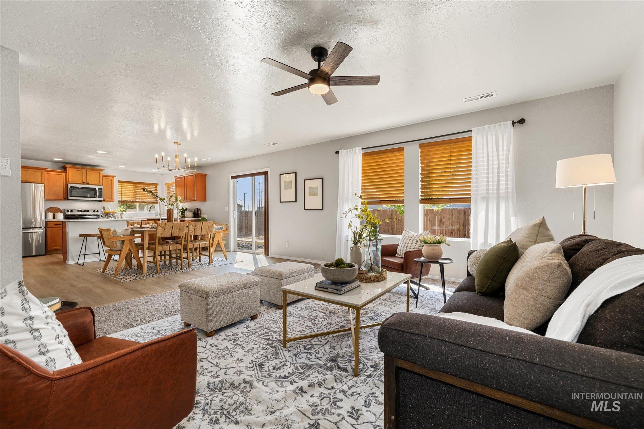 Living room featuring light wood-style flooring, a chandelier, a textured ceiling, and ceiling fan