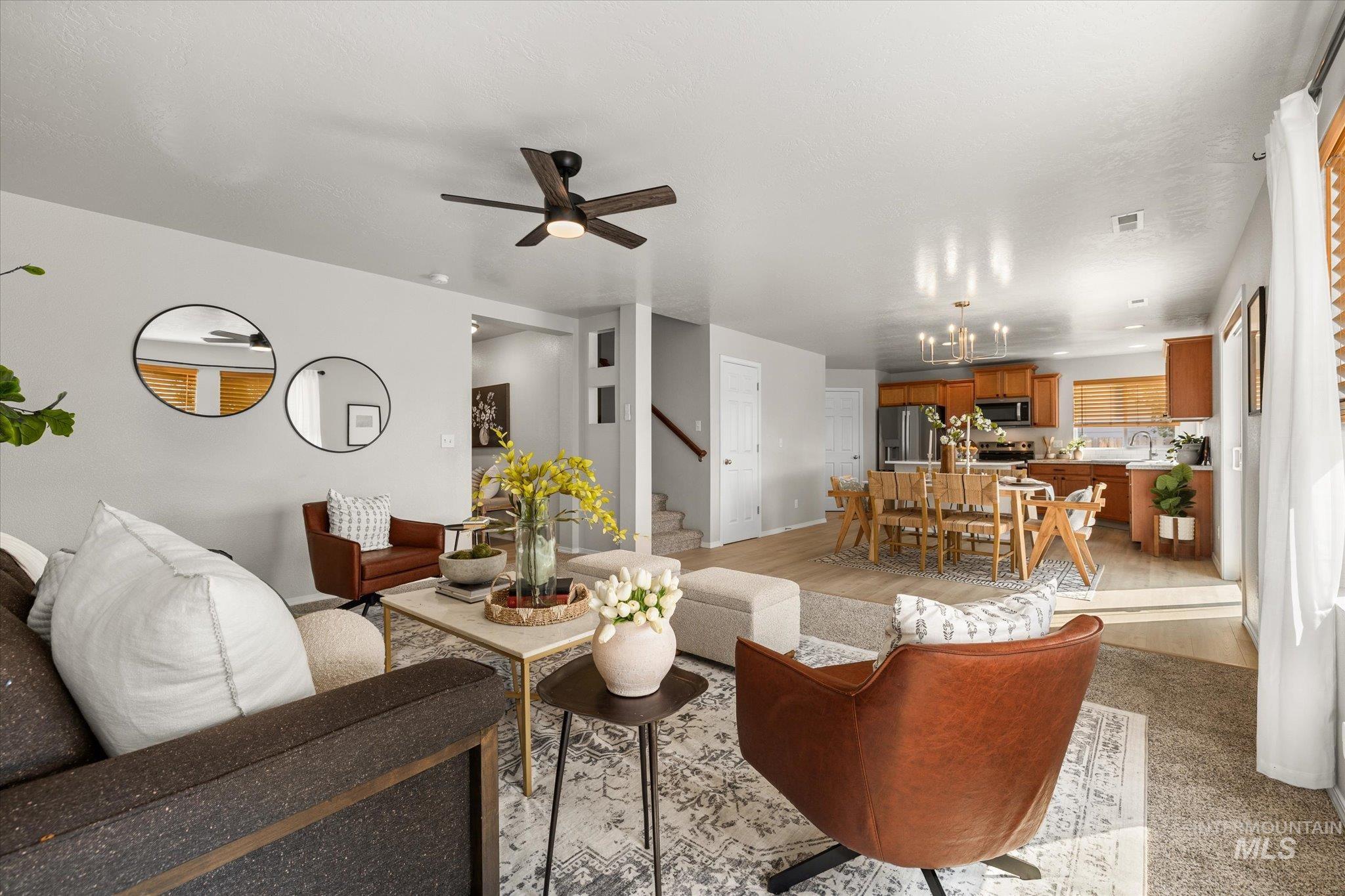 Living room with light wood-type flooring, ceiling fan, stairway, and a chandelier