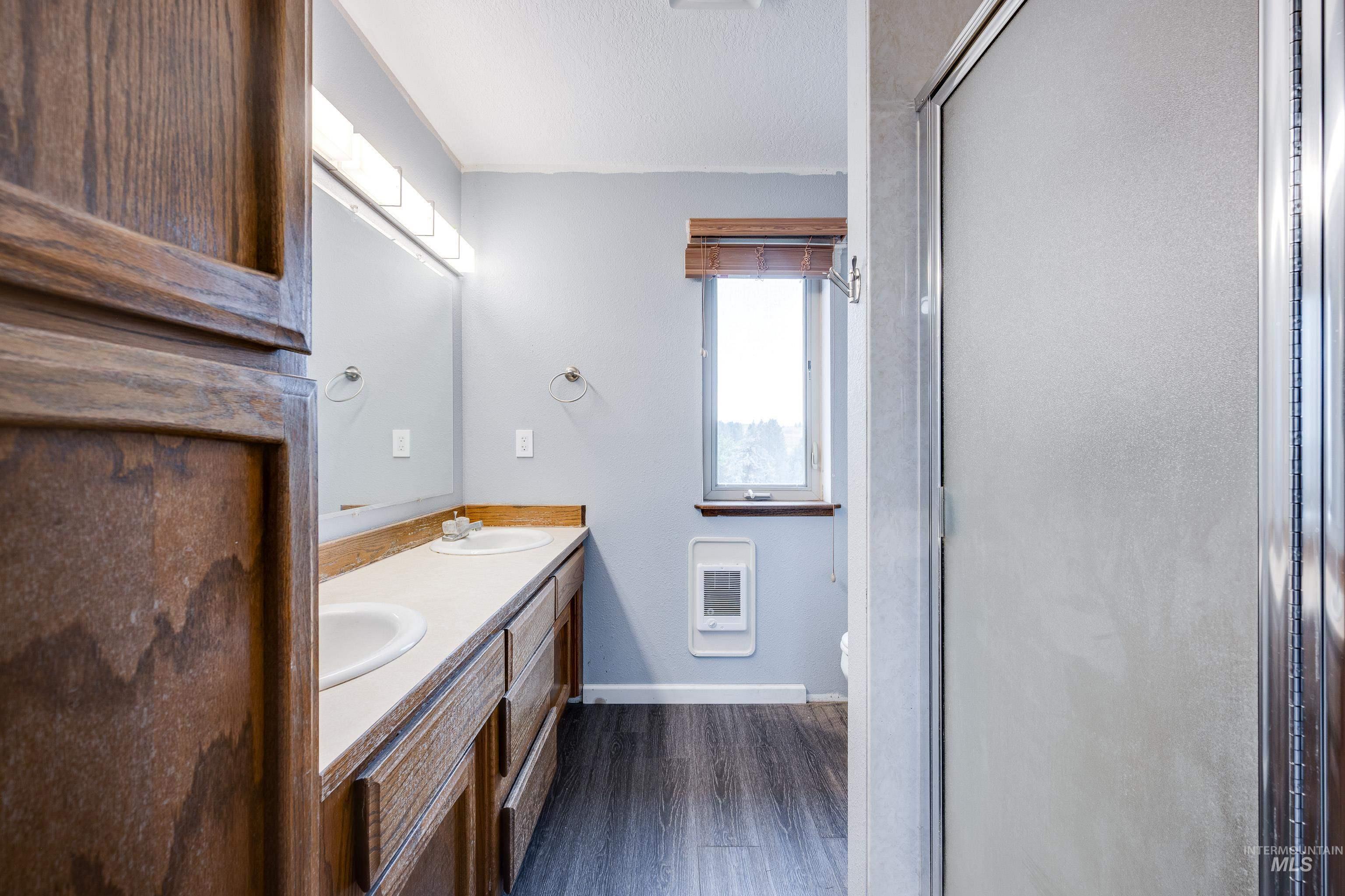Full bathroom with double vanity, dark wood-type flooring, a shower stall, and heating unit
