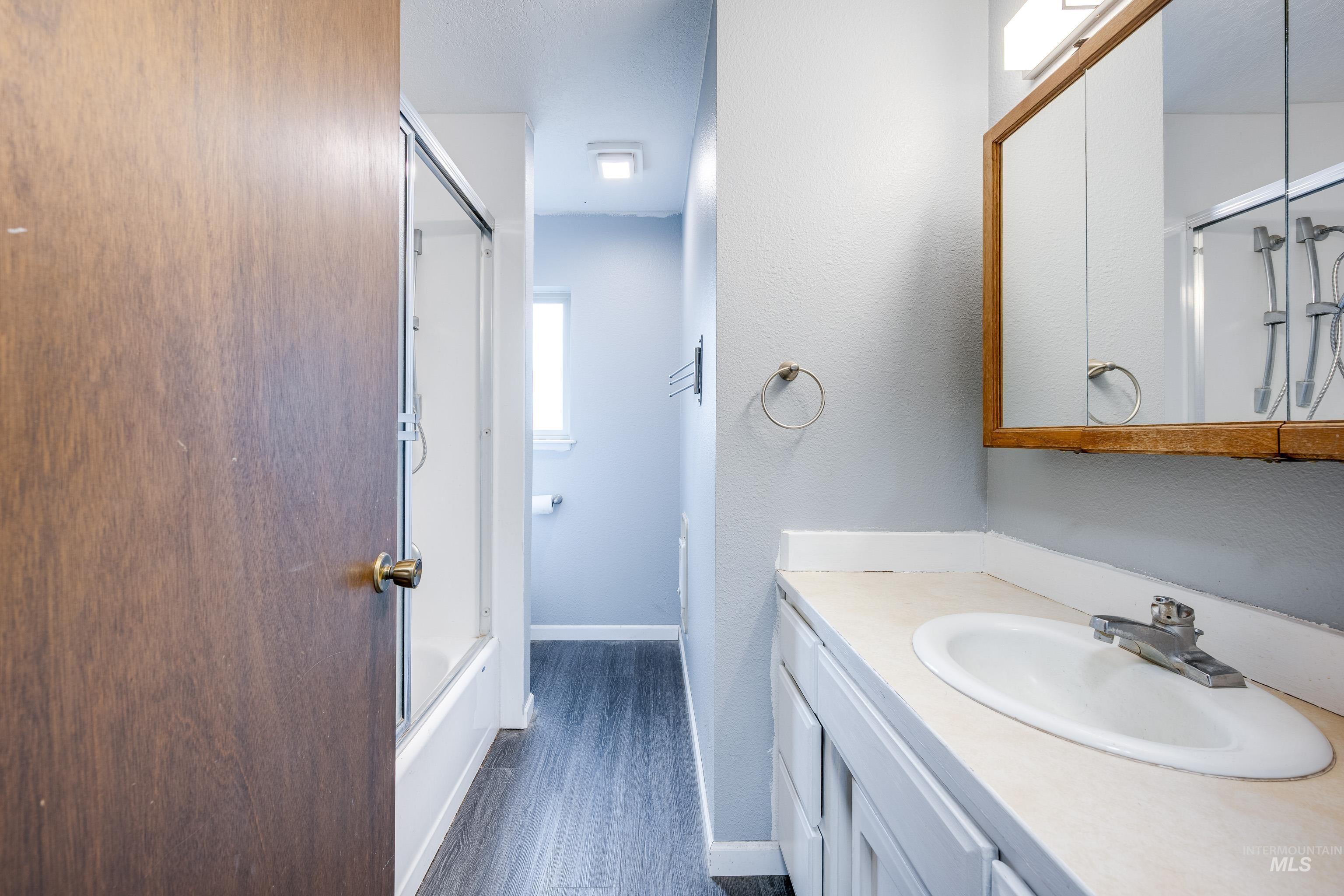 Full bath with shower / bath combination with glass door, vanity, a textured wall, and dark wood-style flooring
