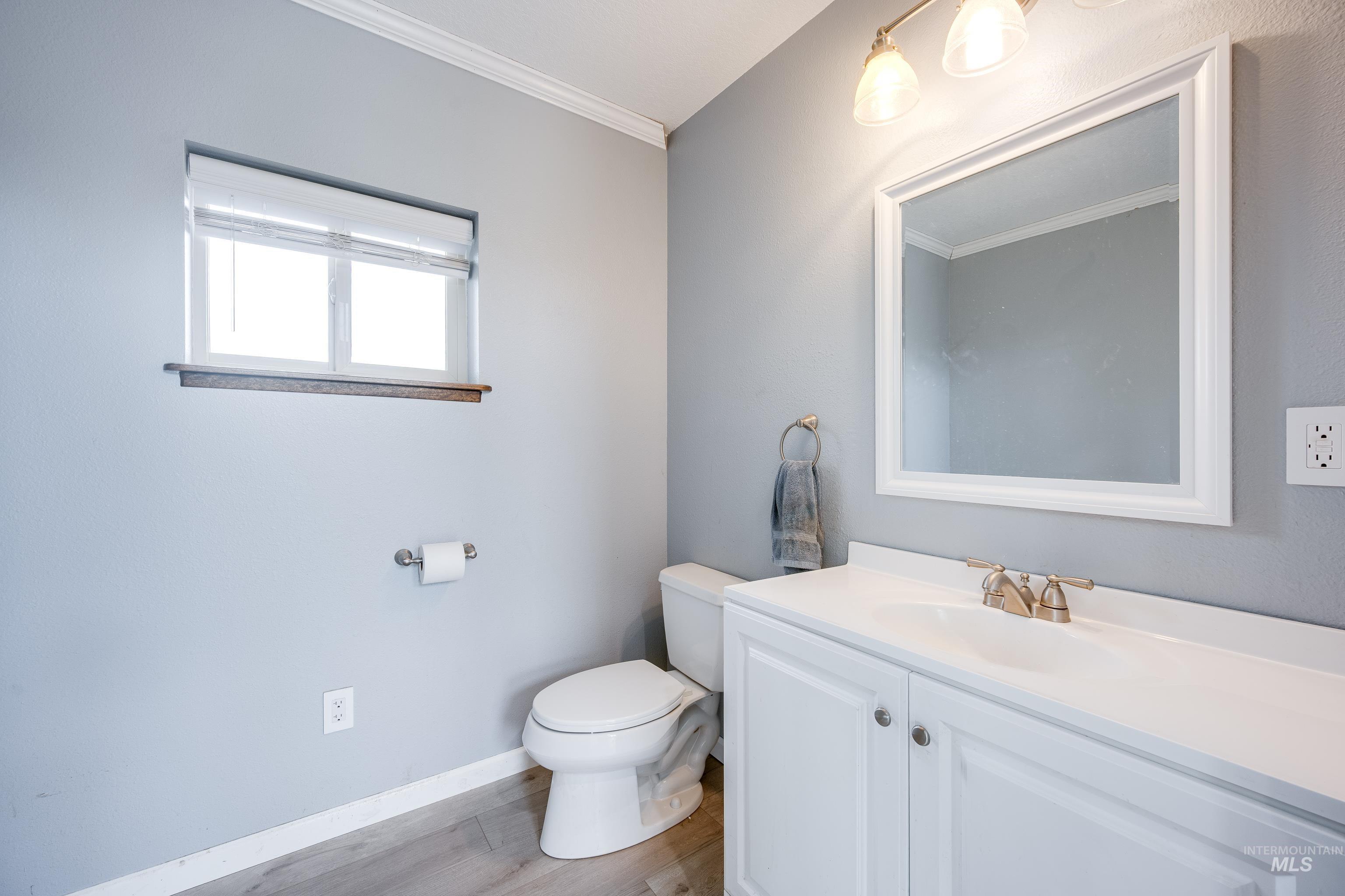 Half bath with vanity, ornamental molding, and light wood-style floors