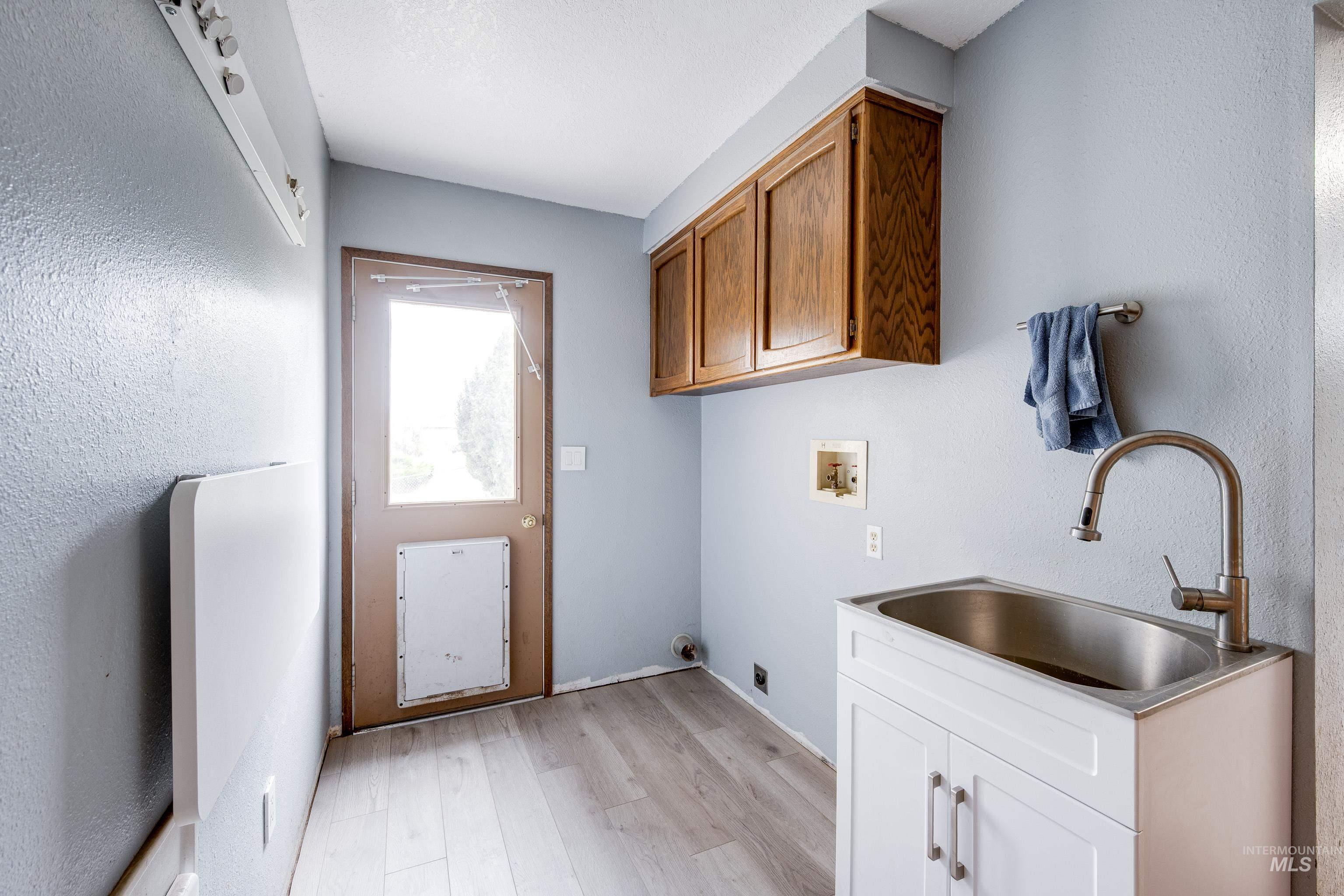 Laundry room featuring cabinet space, light wood-style floors, hookup for a washing machine, a textured wall, and electric dryer hookup