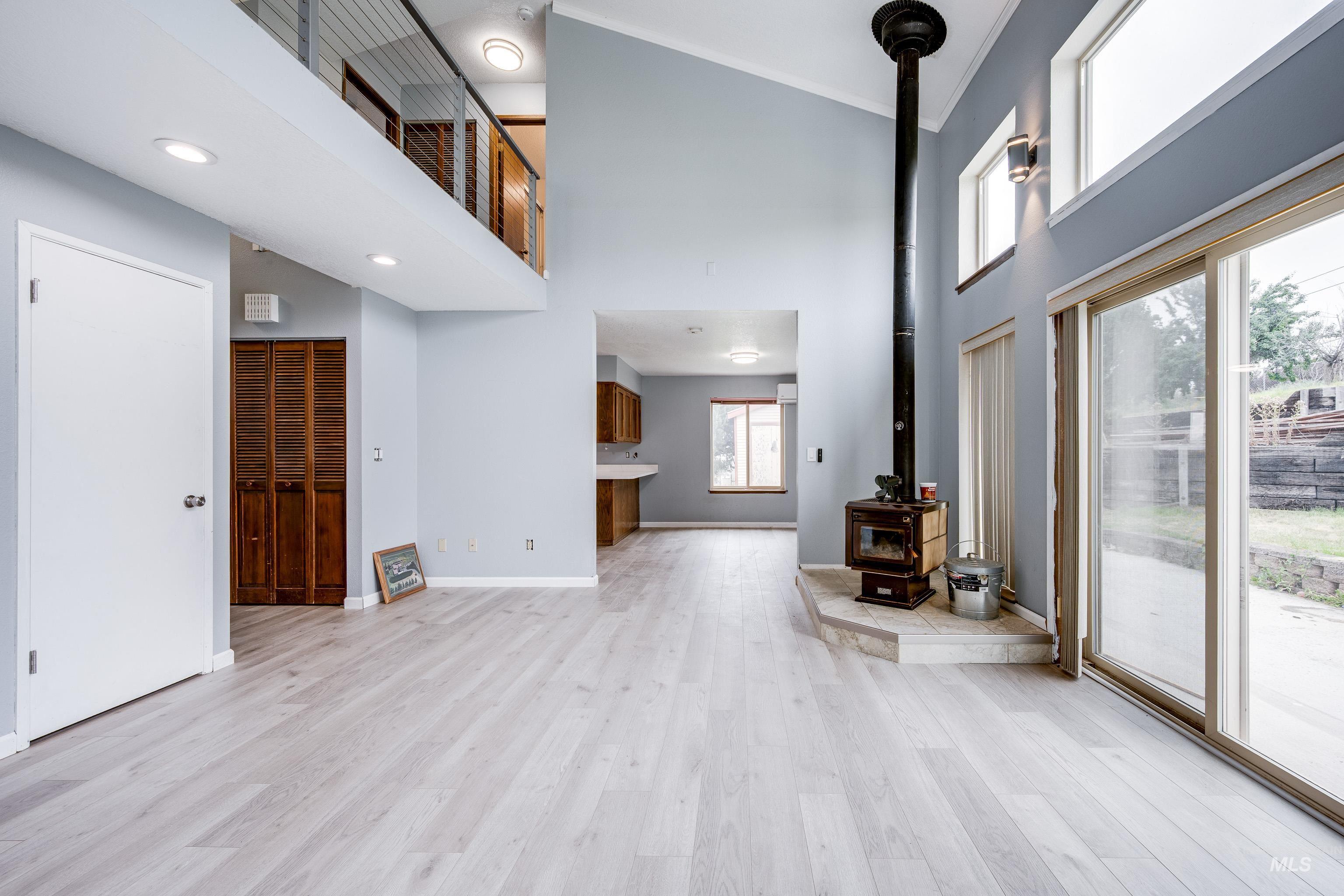 Unfurnished living room featuring a towering ceiling, a wood stove, light wood-style flooring, and ornamental molding