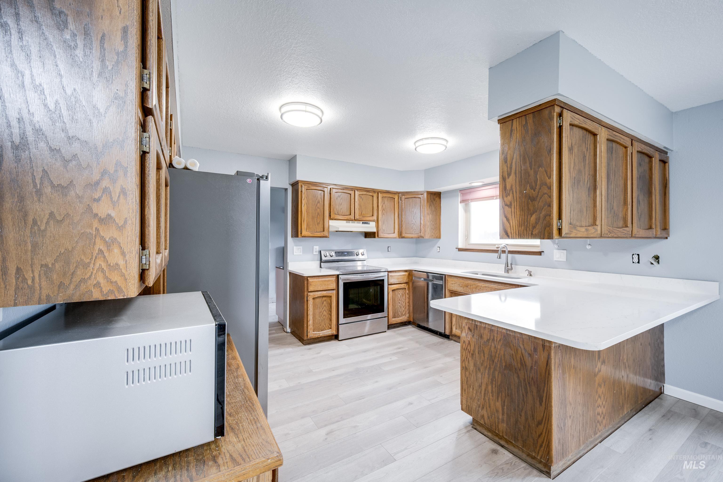 Kitchen featuring brown cabinetry, a peninsula, stainless steel appliances, and light wood-style flooring