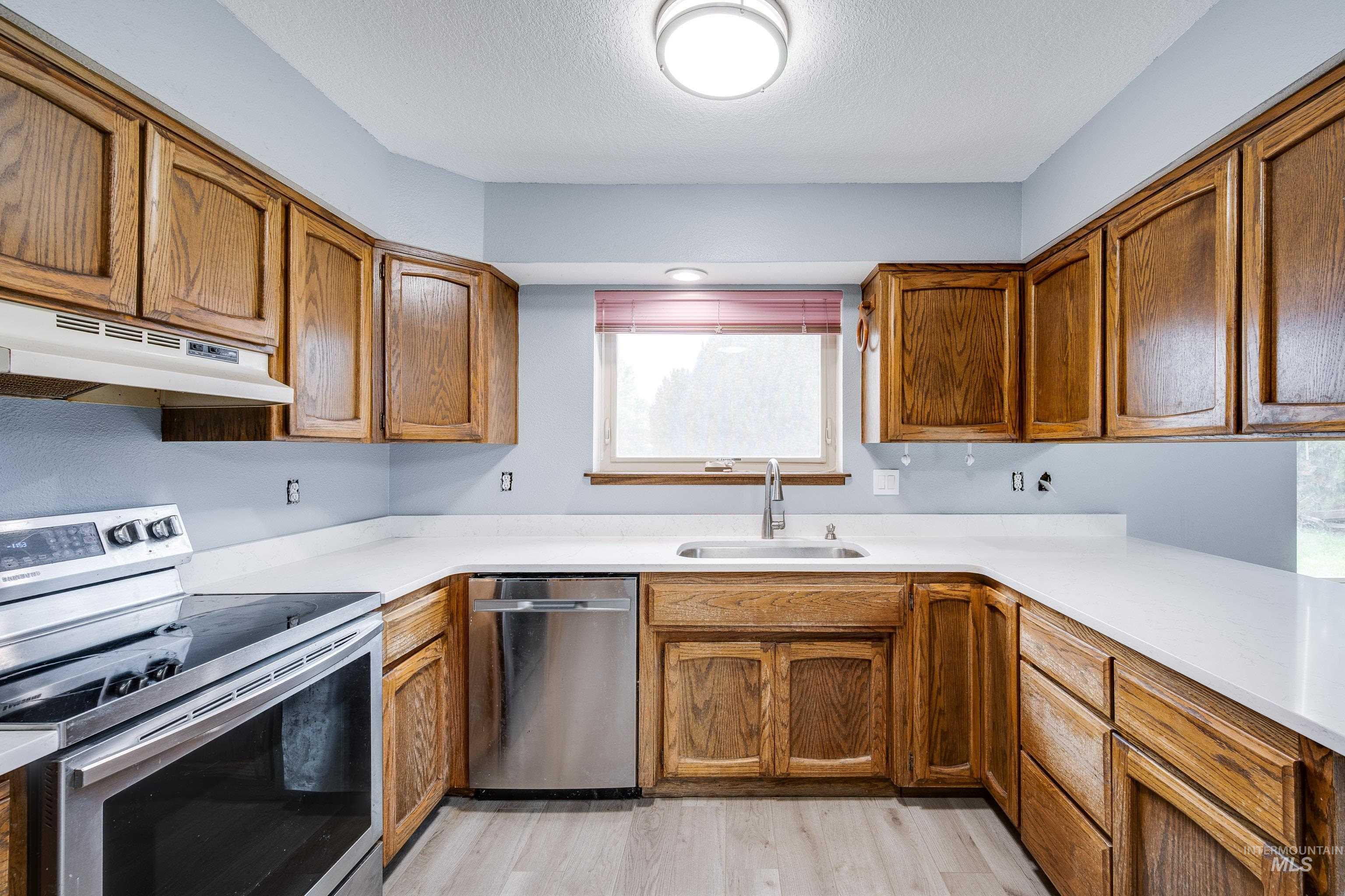 Kitchen featuring appliances with stainless steel finishes, brown cabinets, light wood-style flooring, under cabinet range hood, and a textured ceiling