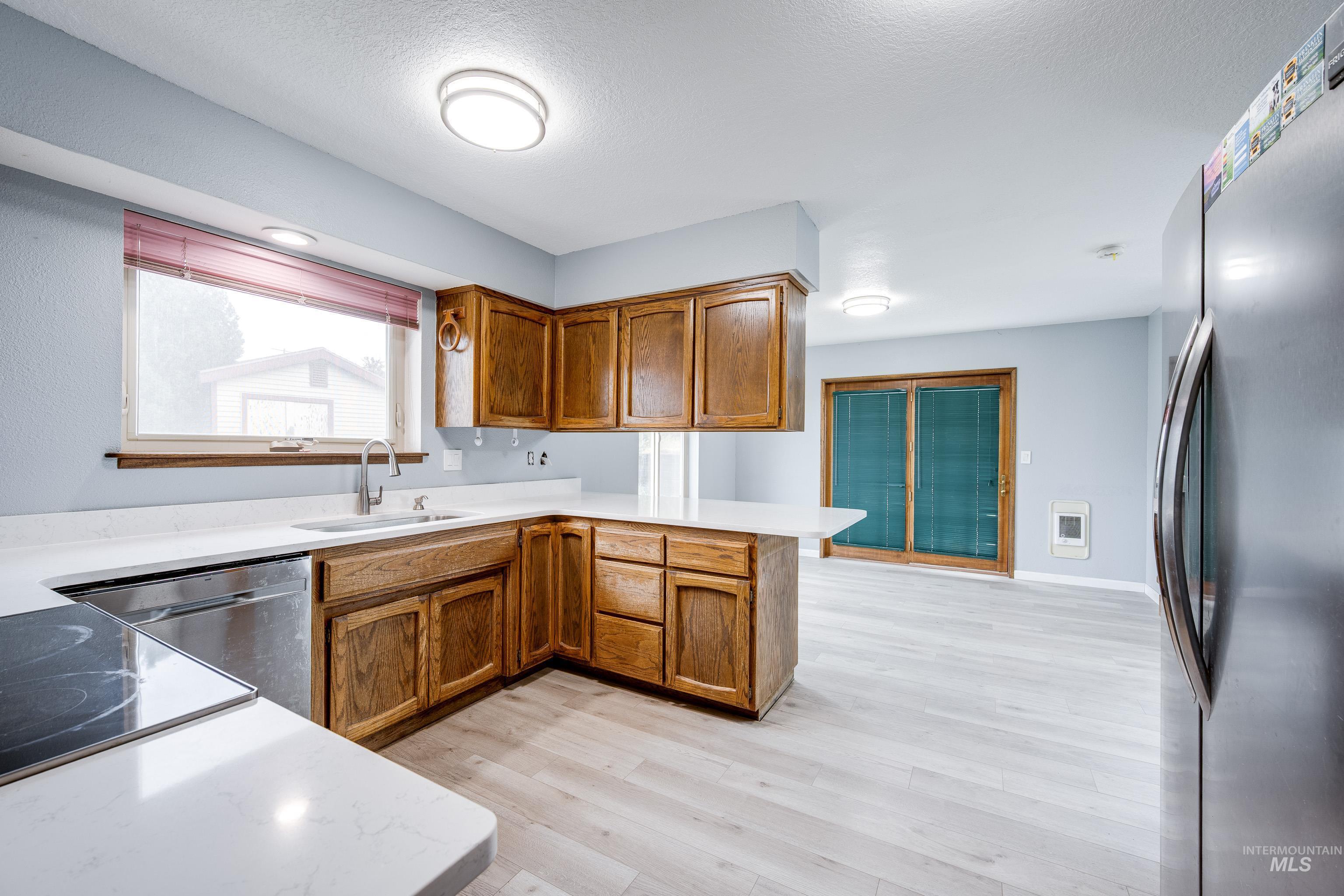 Kitchen with appliances with stainless steel finishes, brown cabinetry, a peninsula, light wood-type flooring, and heating unit