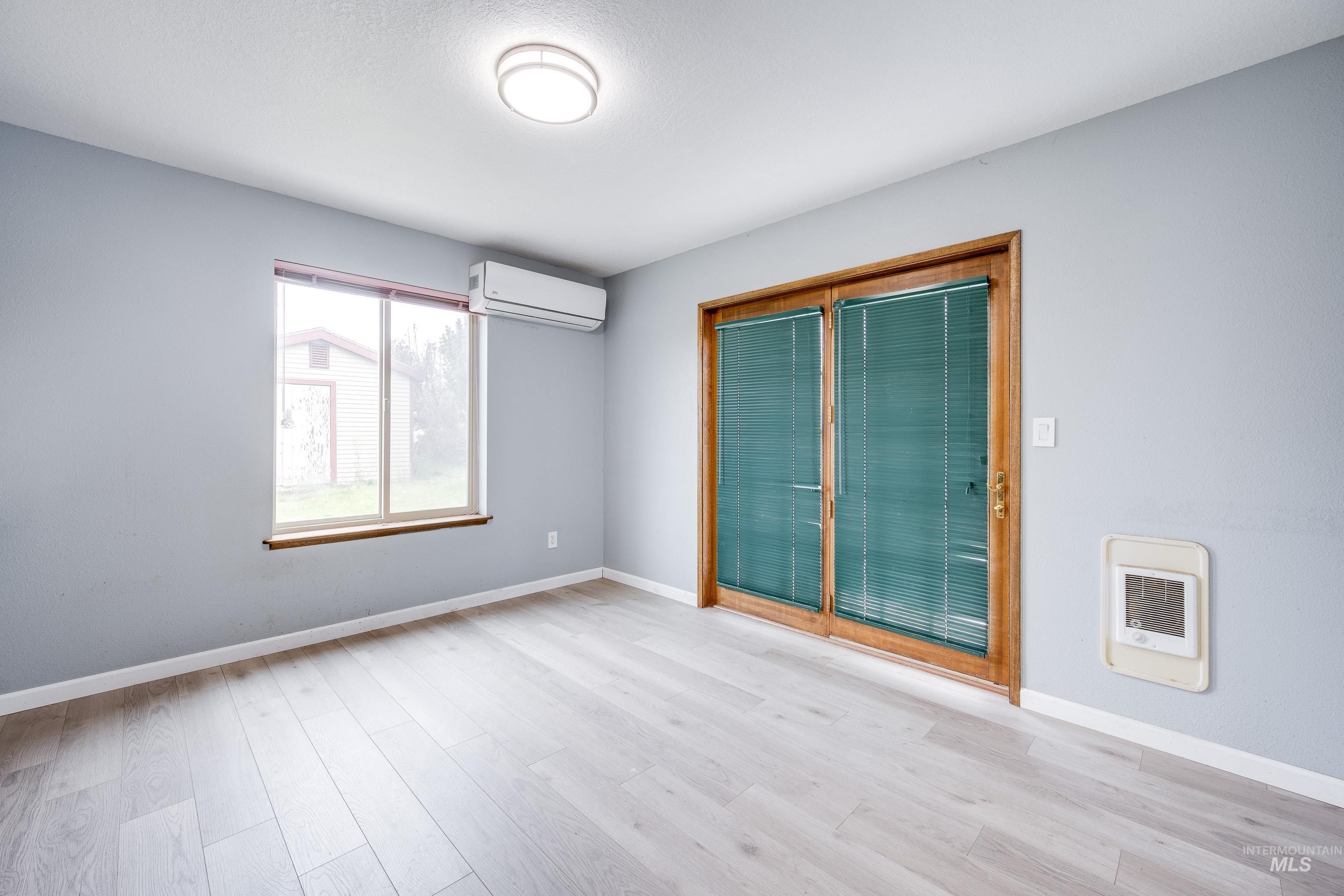Spare room with light wood-style floors, a wall unit AC, and heating unit