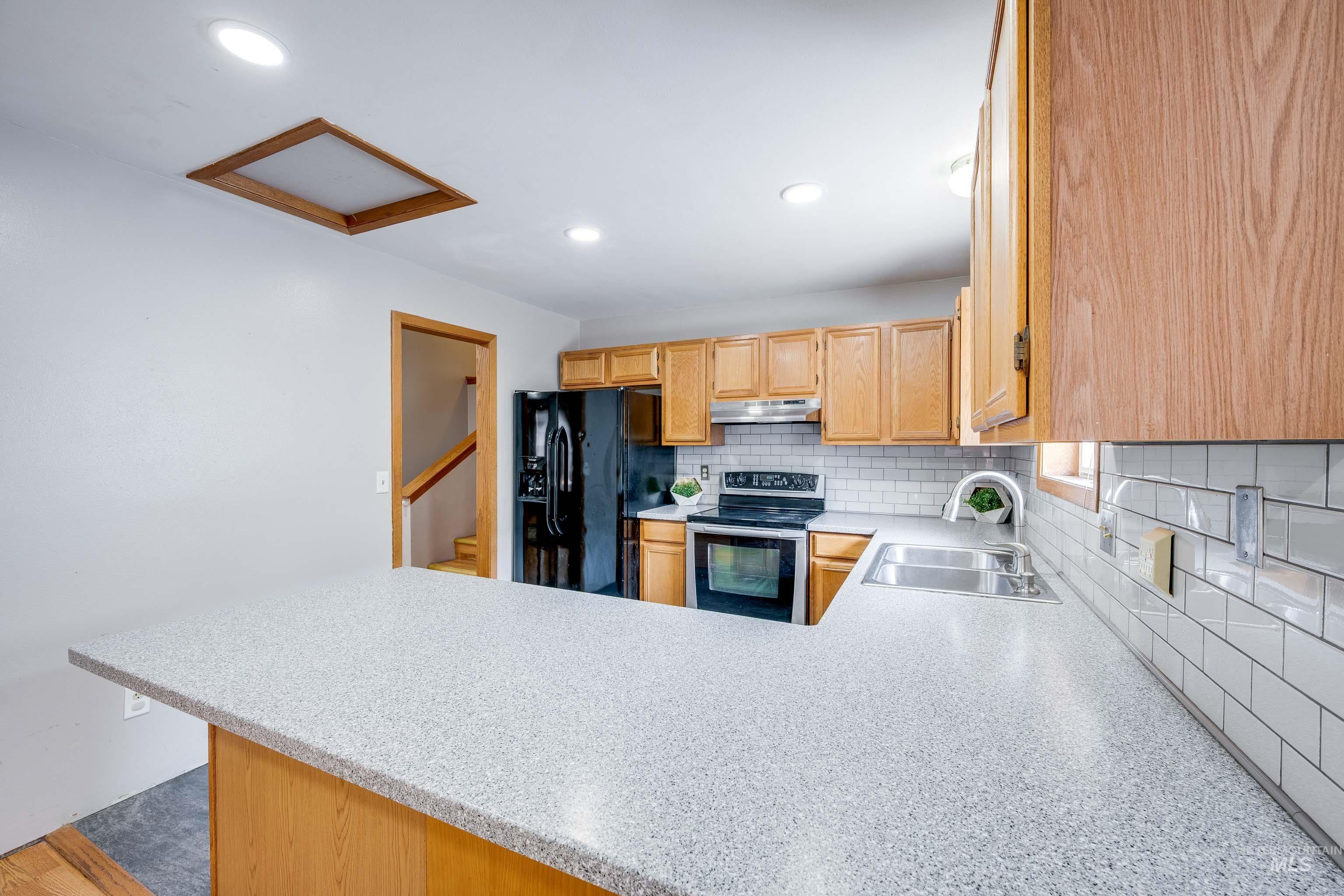 Kitchen featuring backsplash, stainless steel range with electric stovetop, black fridge with ice dispenser, a peninsula, and recessed lighting