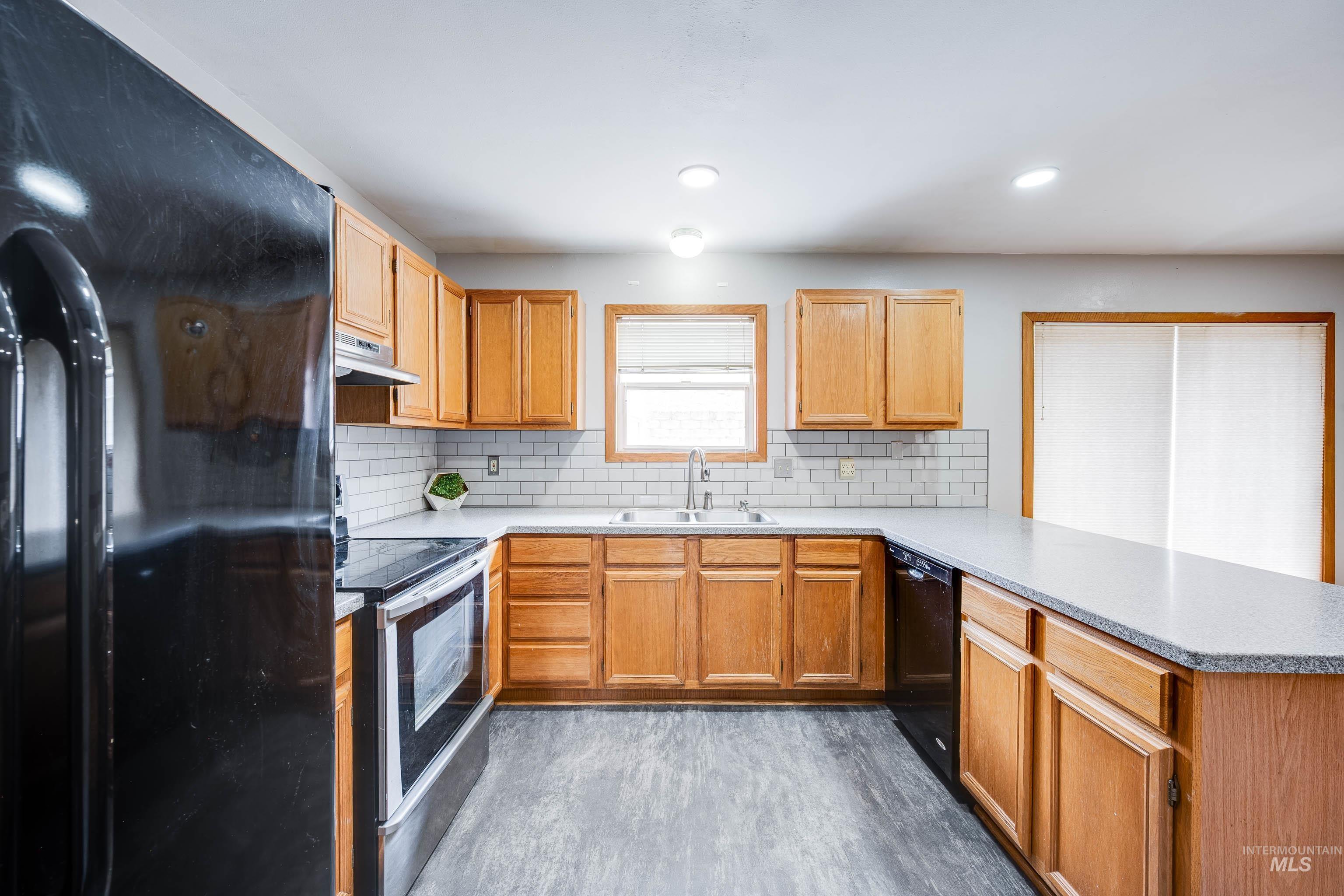 Kitchen featuring black appliances, backsplash, a peninsula, dark wood-style floors, and under cabinet range hood