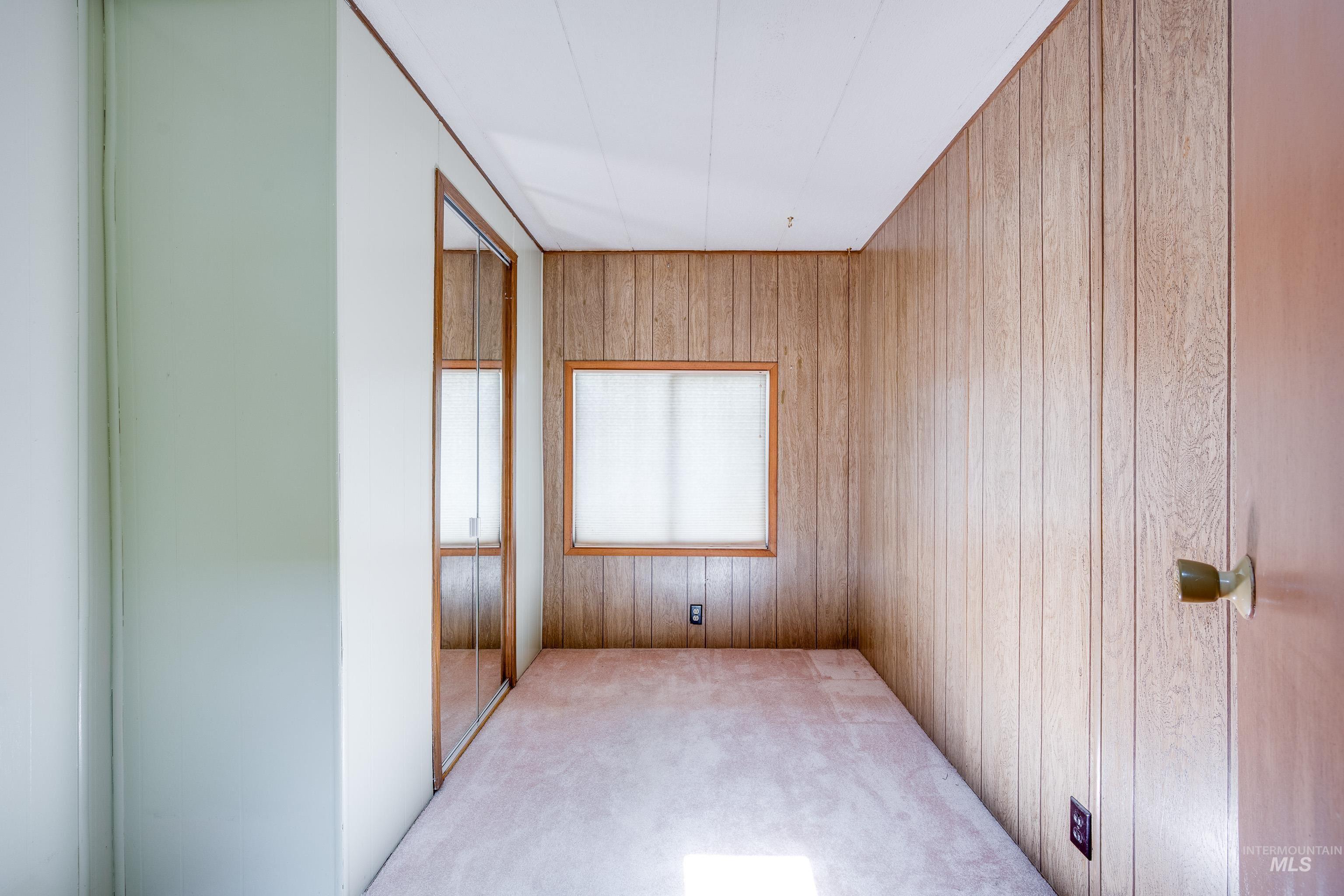 Unfurnished bedroom with carpet, wood walls, and a closet
