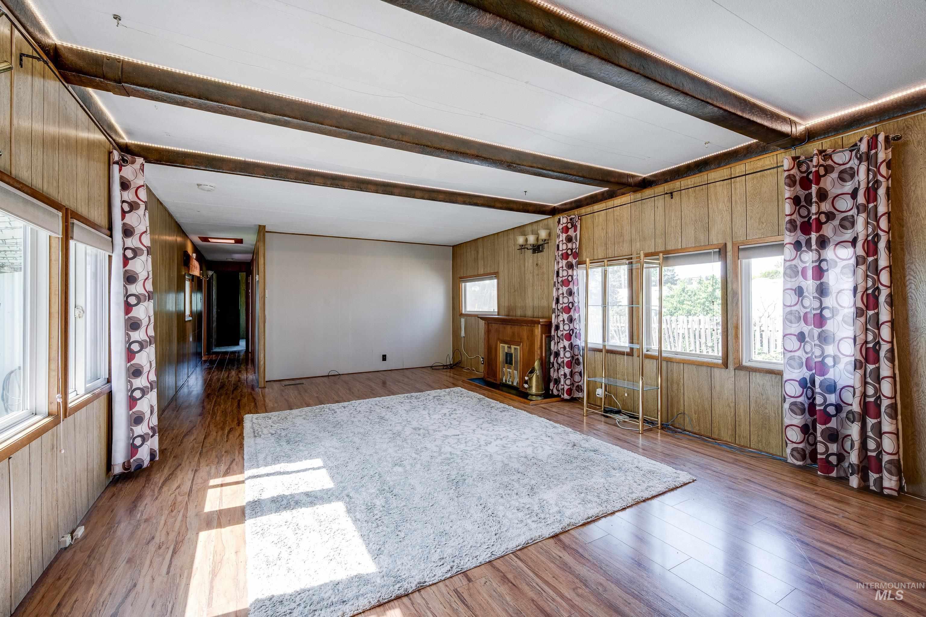 Living room with beamed ceiling, wooden walls, and wood finished floors