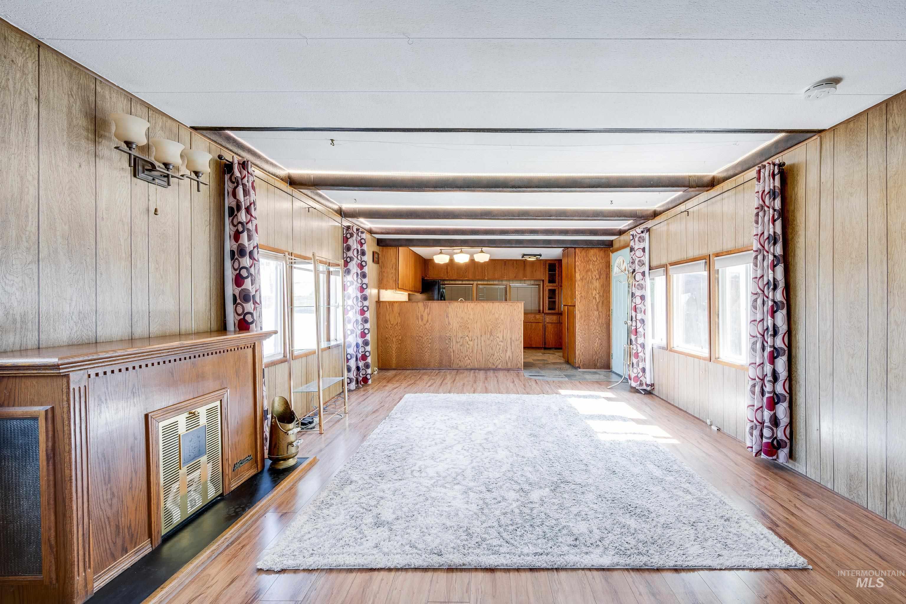 Unfurnished living room with wood walls, light wood-style floors, beamed ceiling, and heating unit
