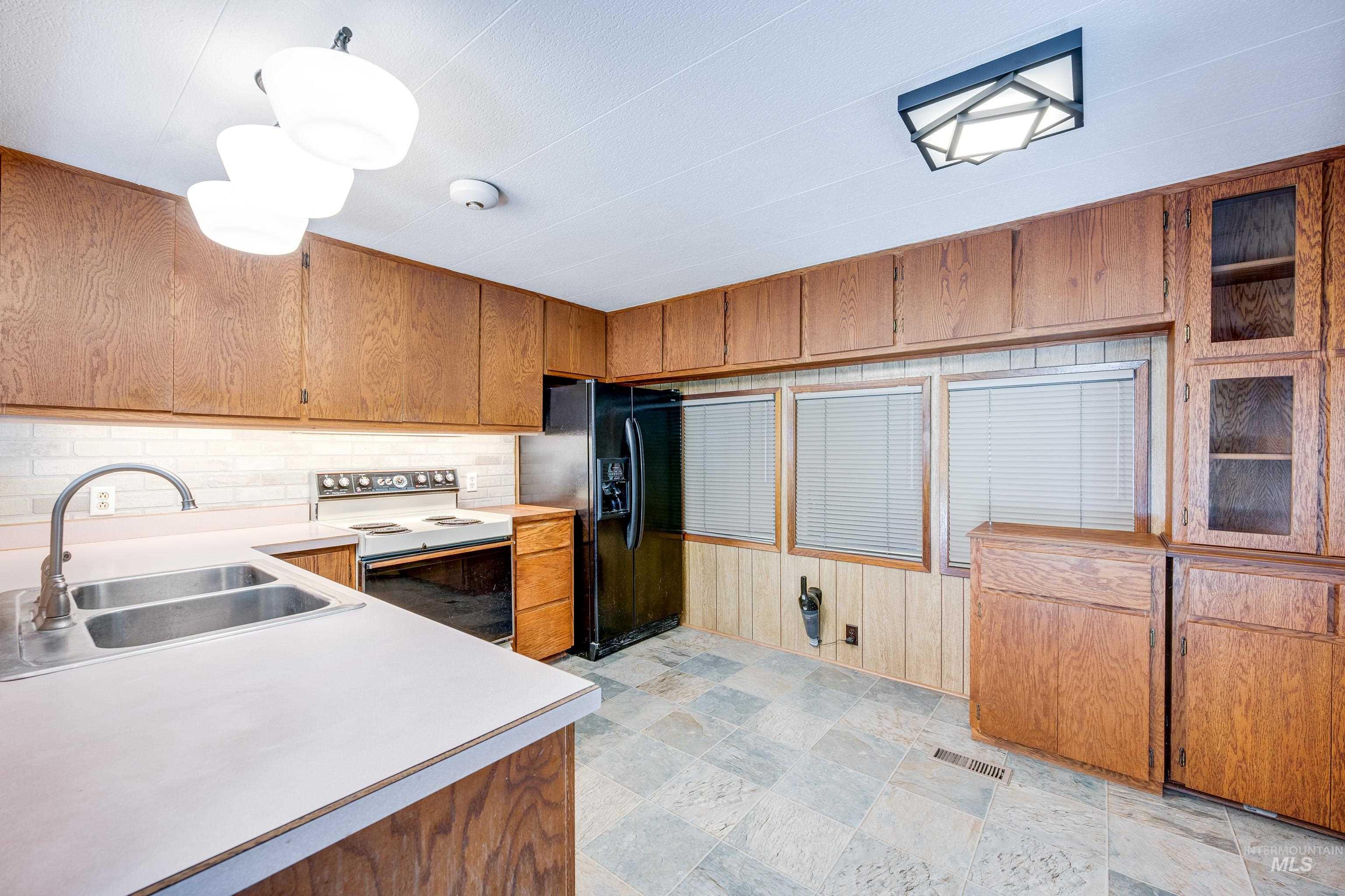 Kitchen with brown cabinets, white range with electric cooktop, black refrigerator with ice dispenser, light countertops, and backsplash