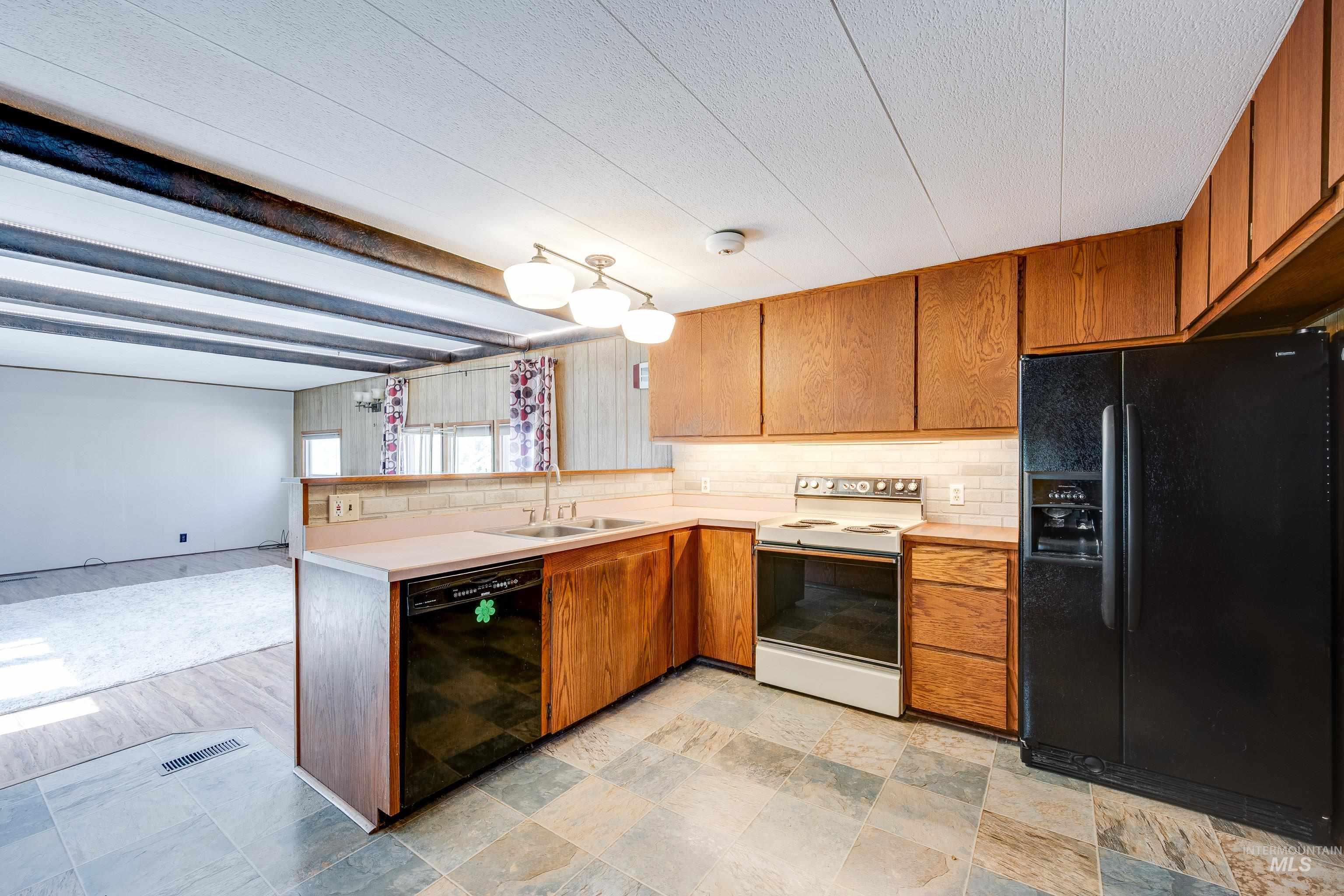 Kitchen featuring black appliances, light countertops, tasteful backsplash, a peninsula, and beamed ceiling