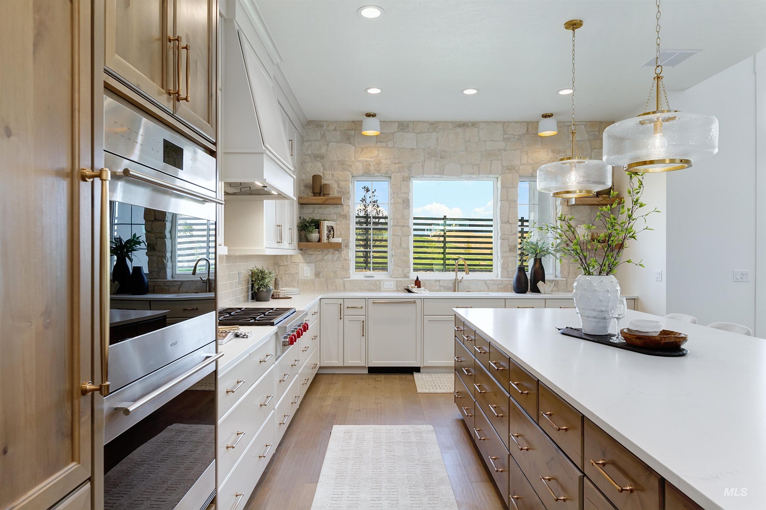 Kitchen with stainless steel appliances, light wood finished floors, pendant lighting, white cabinetry, and backsplash