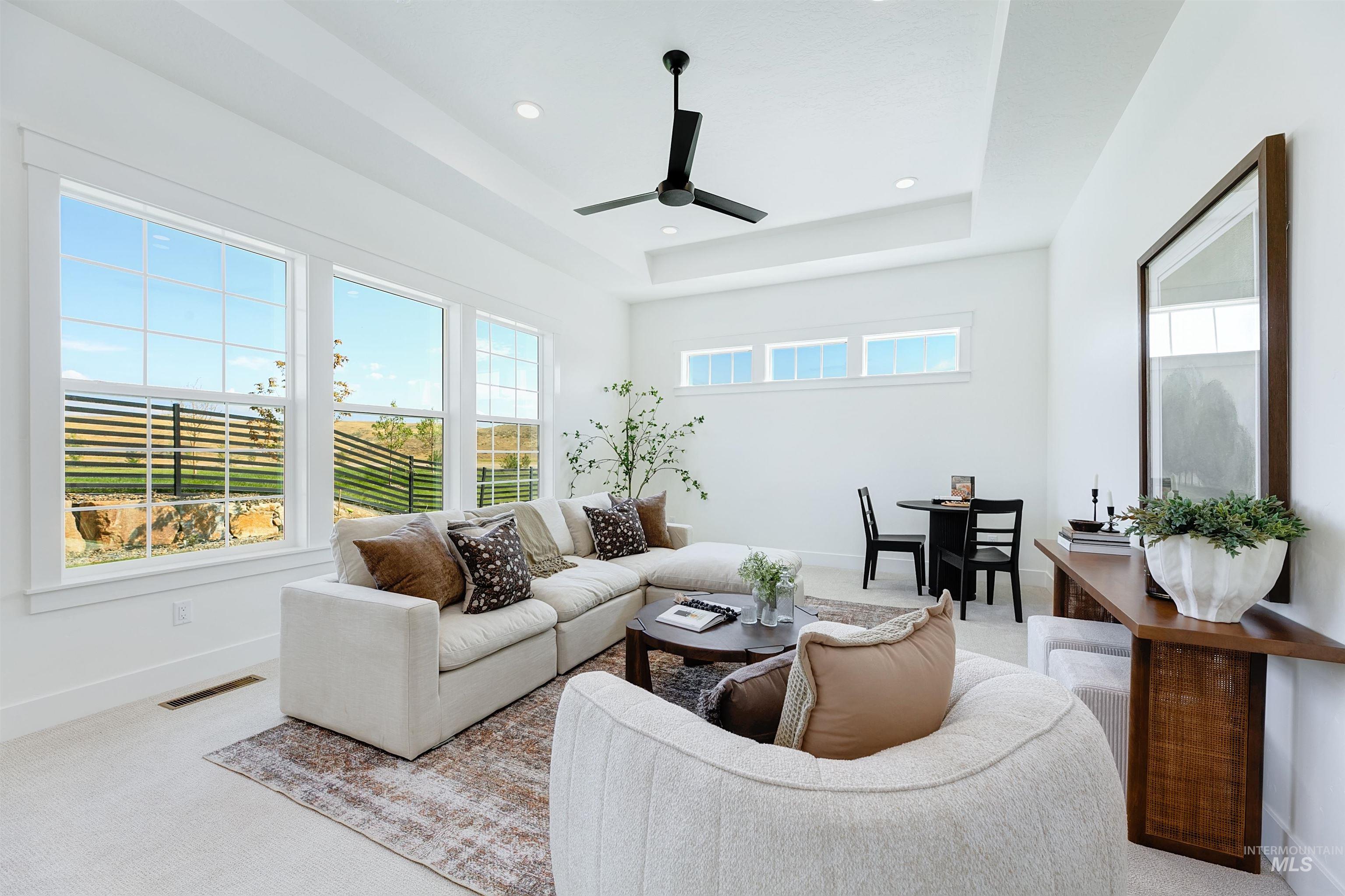 Carpeted living room featuring a raised ceiling, a ceiling fan, and recessed lighting