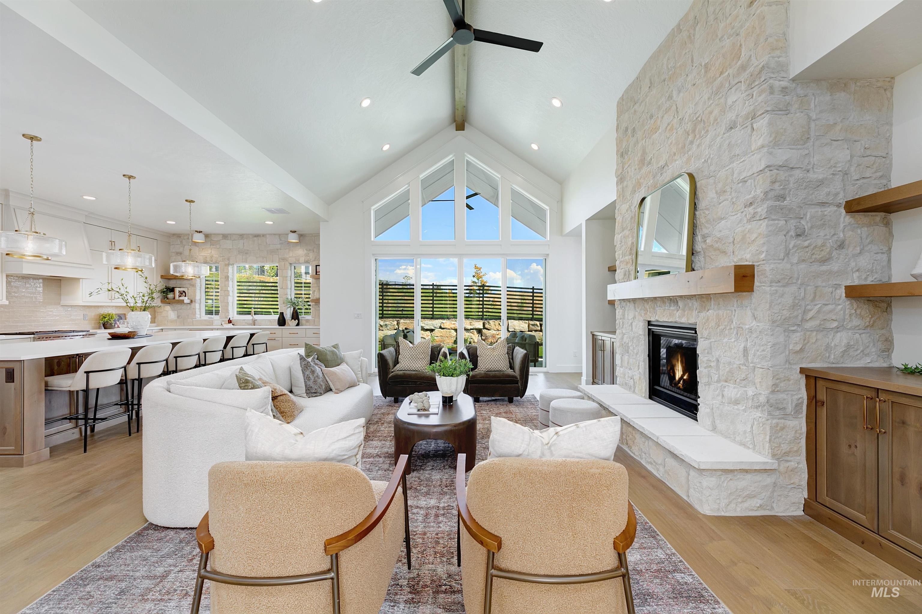 Living area featuring beamed ceiling, light wood-style floors, high vaulted ceiling, a stone fireplace, and ceiling fan