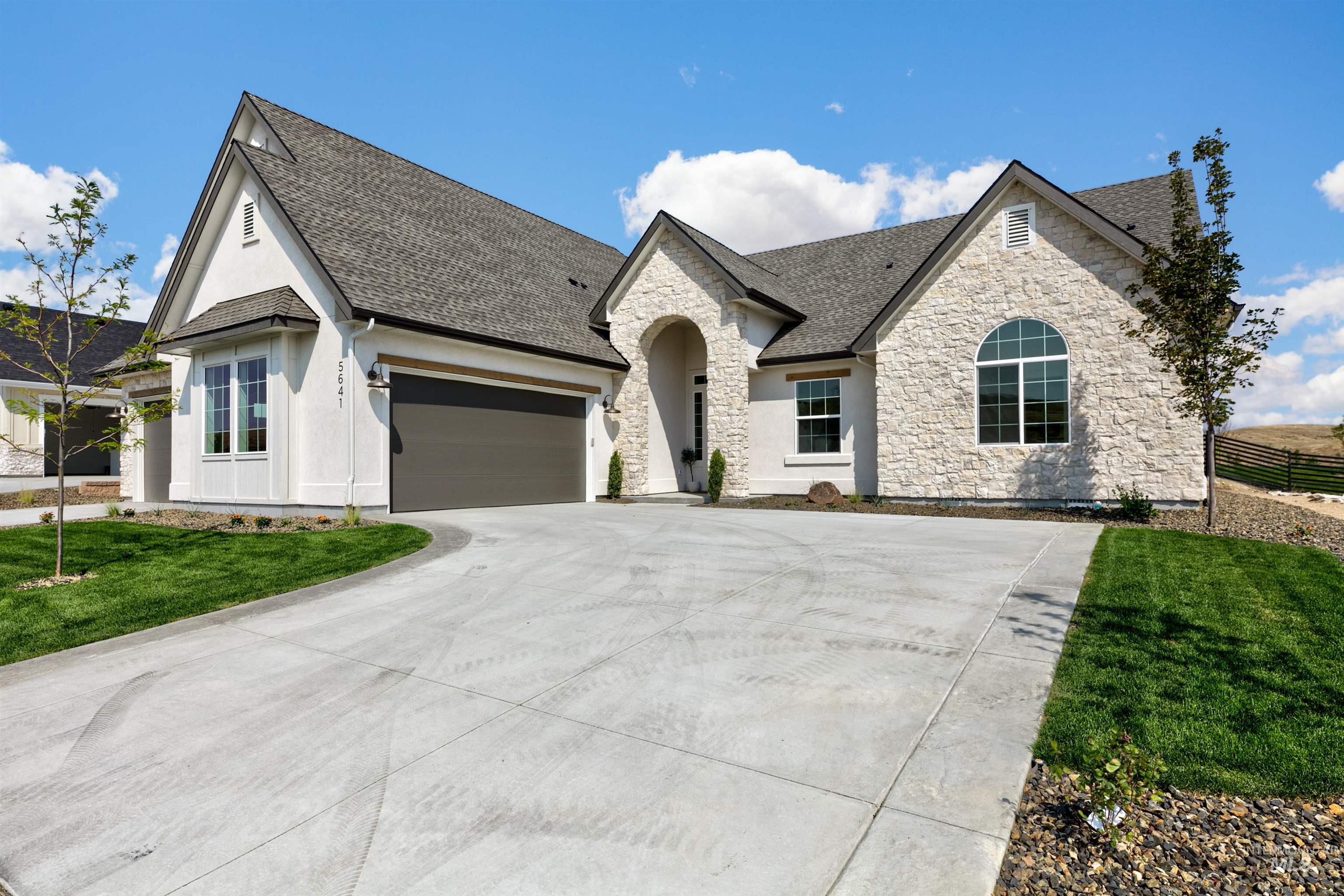 French provincial home featuring stone siding, driveway, a front yard, a shingled roof, and stucco siding