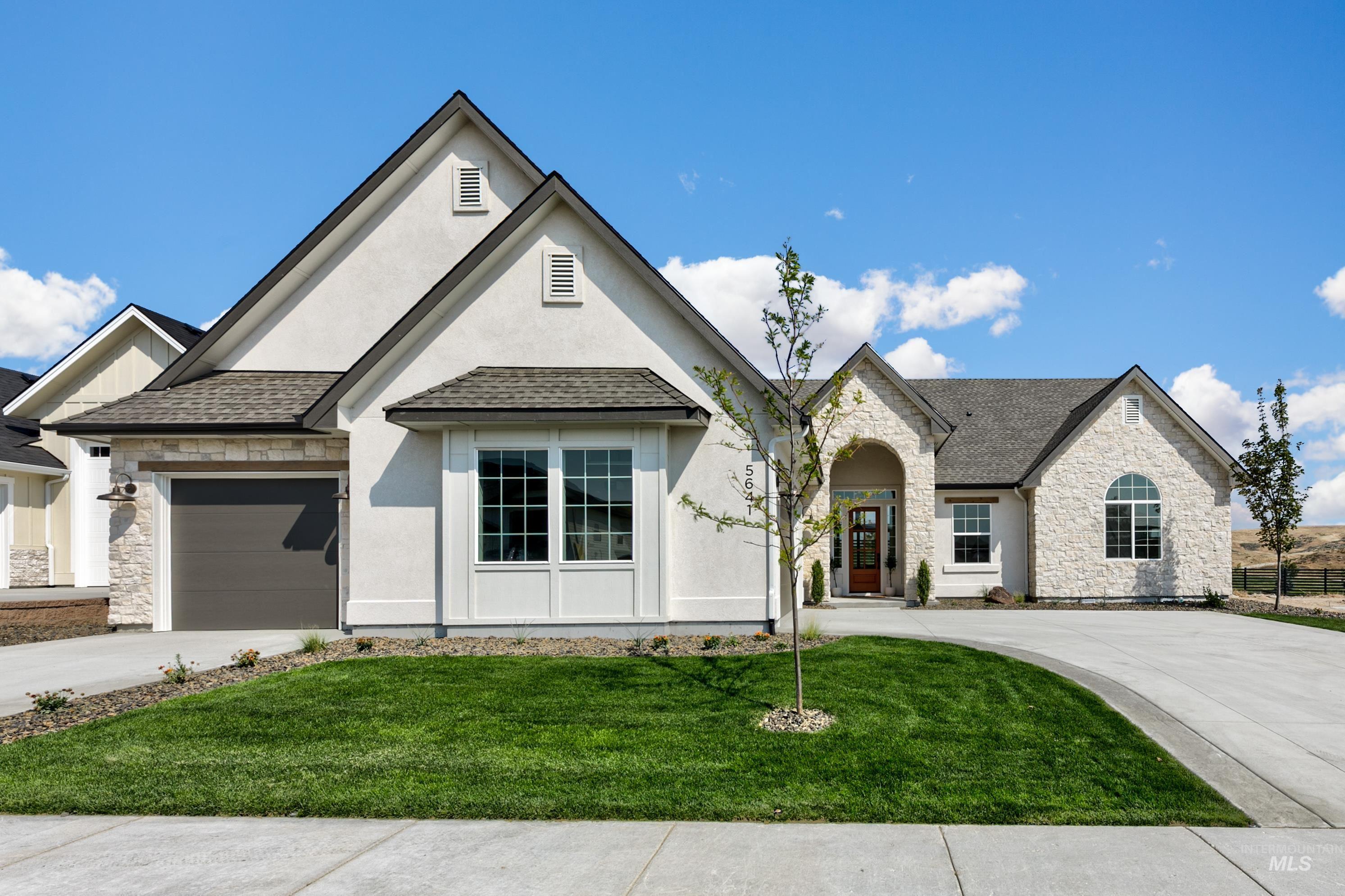 View of front of house featuring stone siding, driveway, a front yard, and a shingled roof