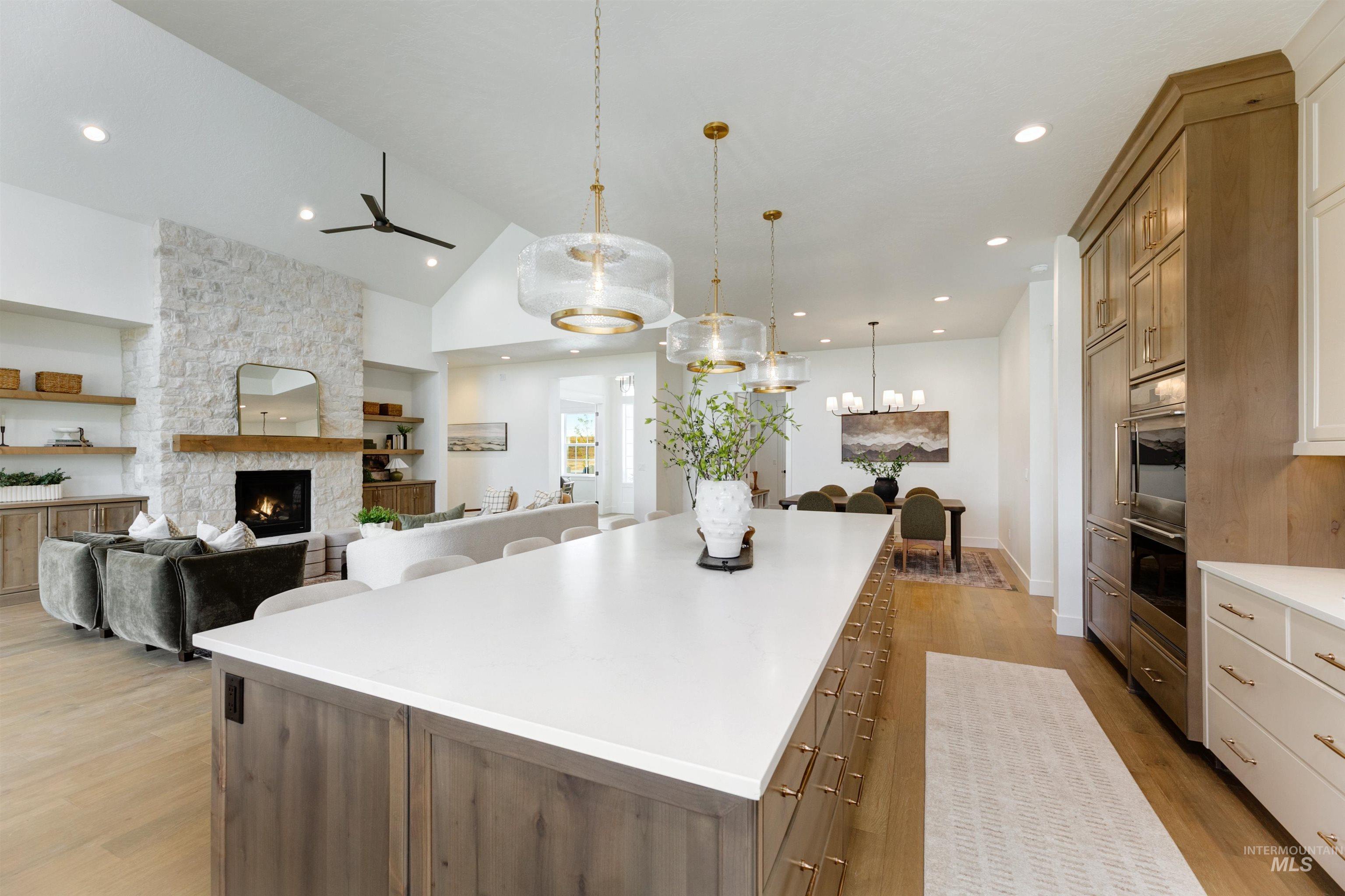 Kitchen featuring light wood-style floors, a stone fireplace, open floor plan, a ceiling fan, and decorative light fixtures