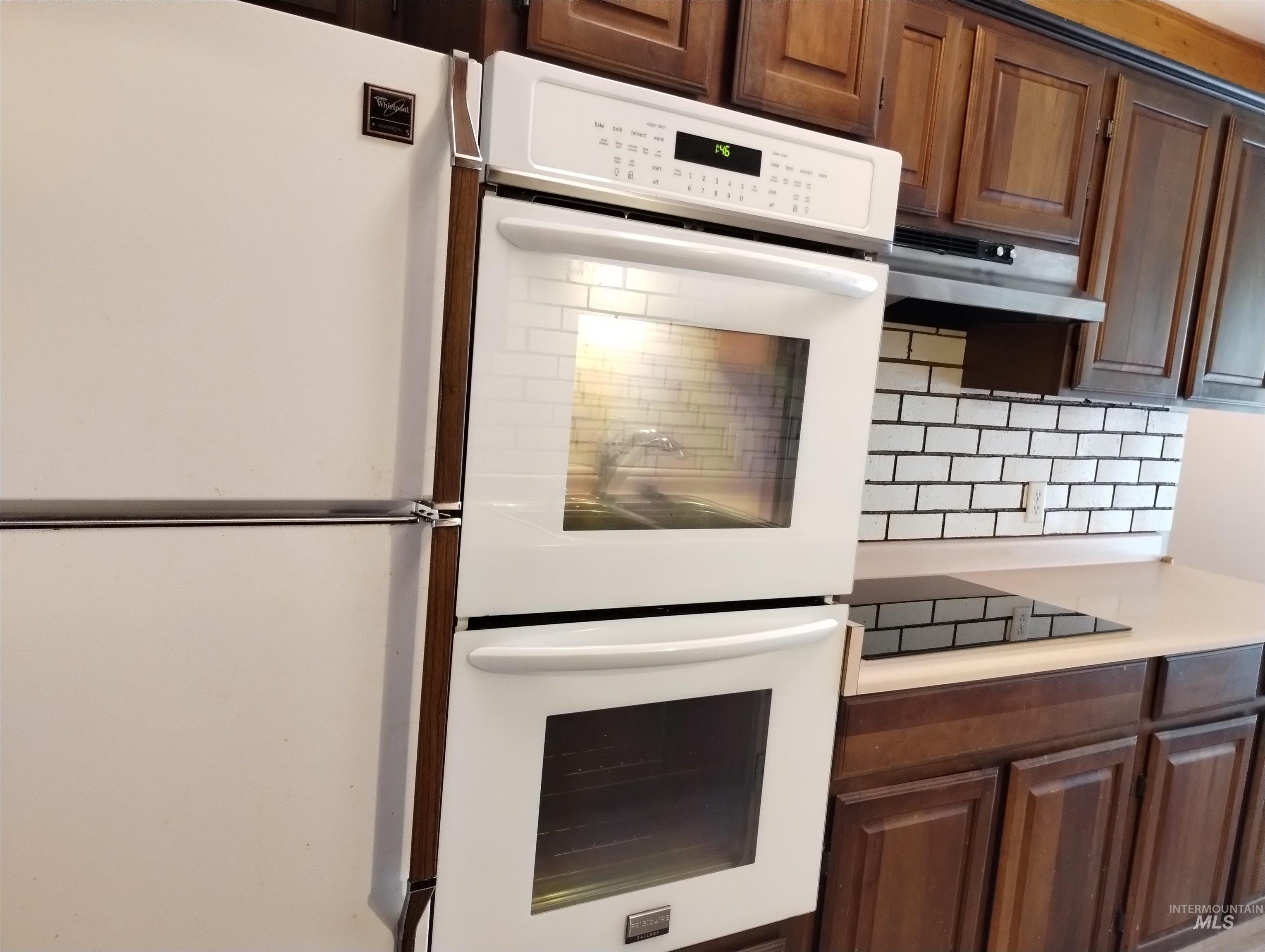 Kitchen featuring white appliances, light countertops, tasteful backsplash, under cabinet range hood, and dark brown cabinets