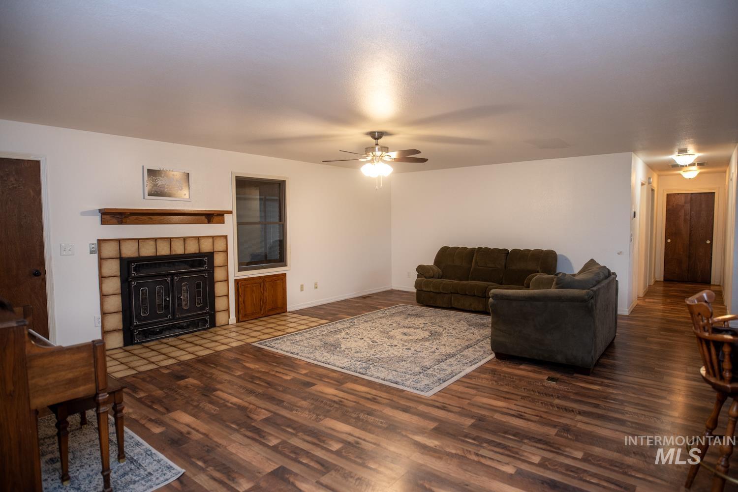 Living area featuring dark wood-style flooring, a ceiling fan, and a tile fireplace