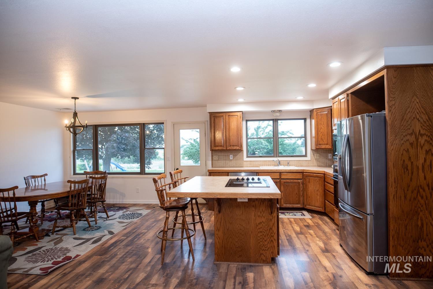 Kitchen with light countertops, tasteful backsplash, stainless steel fridge, dark wood finished floors, and brown cabinetry