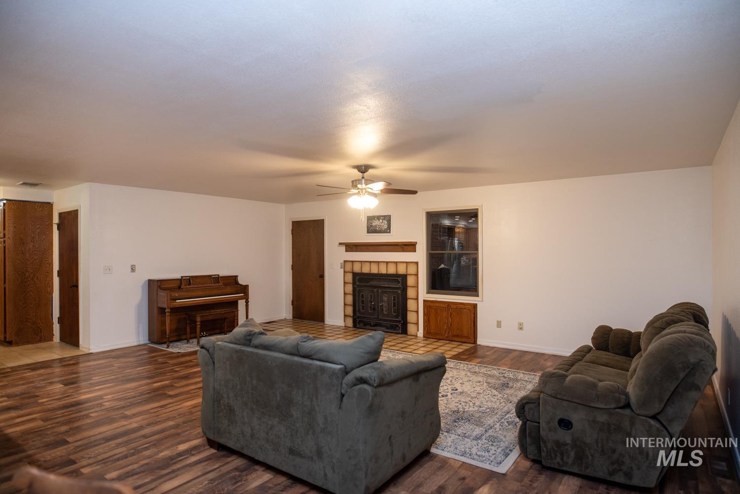 Living room featuring dark wood-style flooring, a tiled fireplace, and a ceiling fan