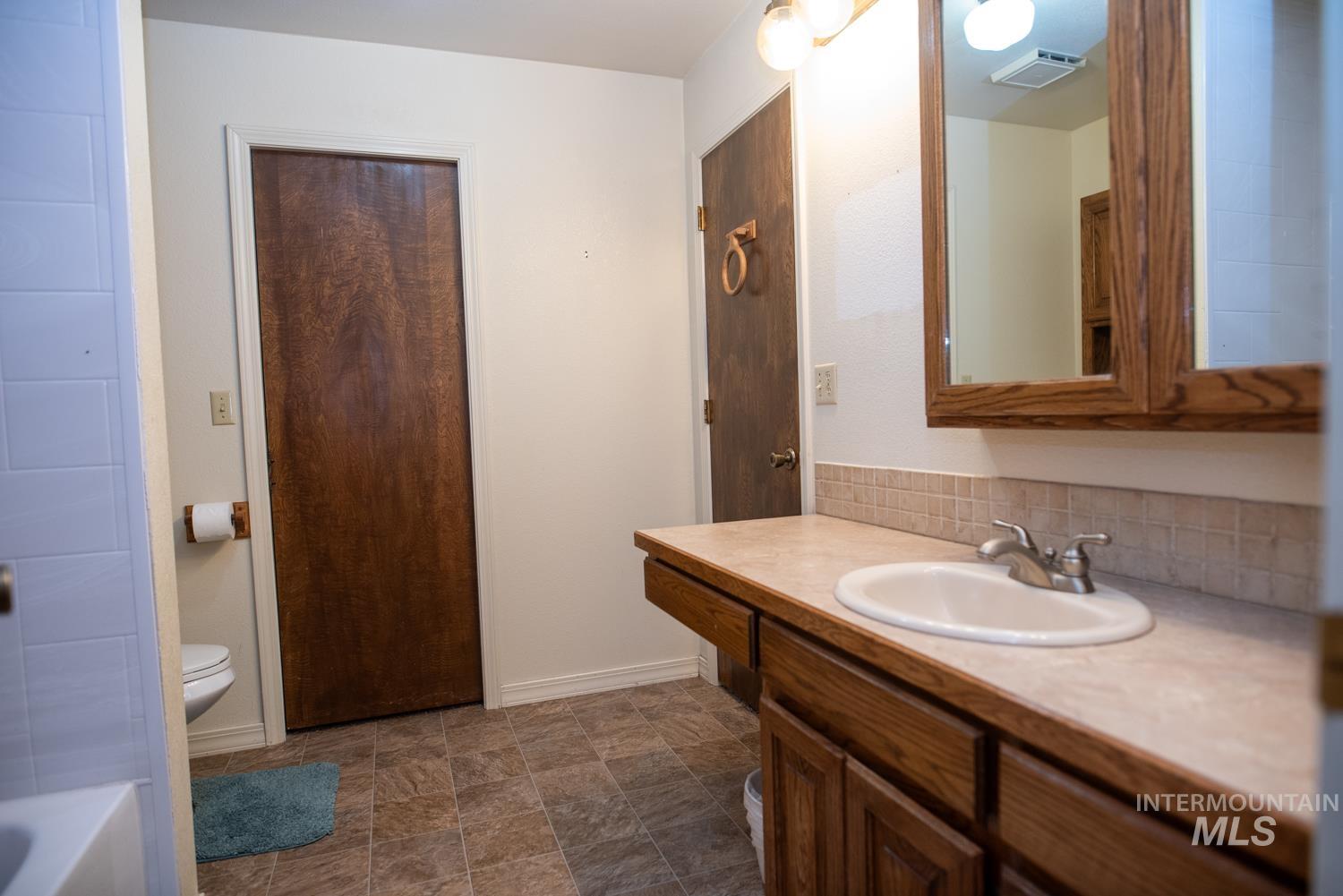 Full bath with vanity, a tub to relax in, decorative backsplash, and stone finish floors