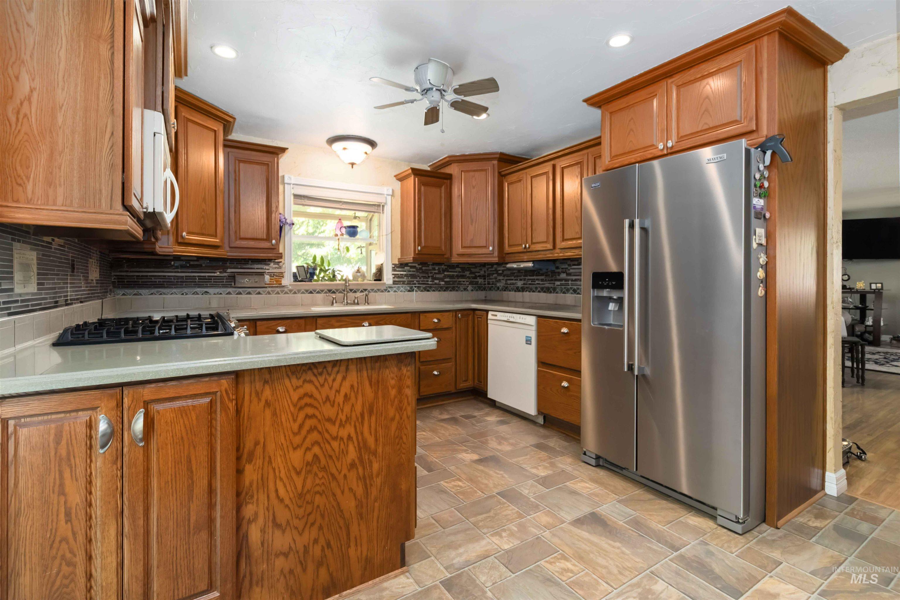 Kitchen with white appliances, brown cabinets, a ceiling fan, light stone finish flooring, and tasteful backsplash
