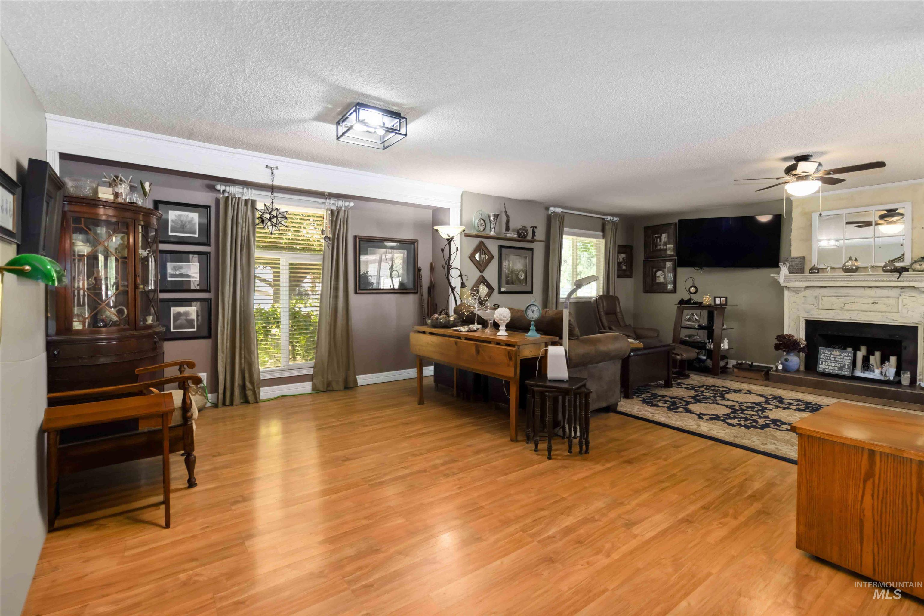Living area with a textured ceiling, a fireplace, light wood-style floors, and ceiling fan