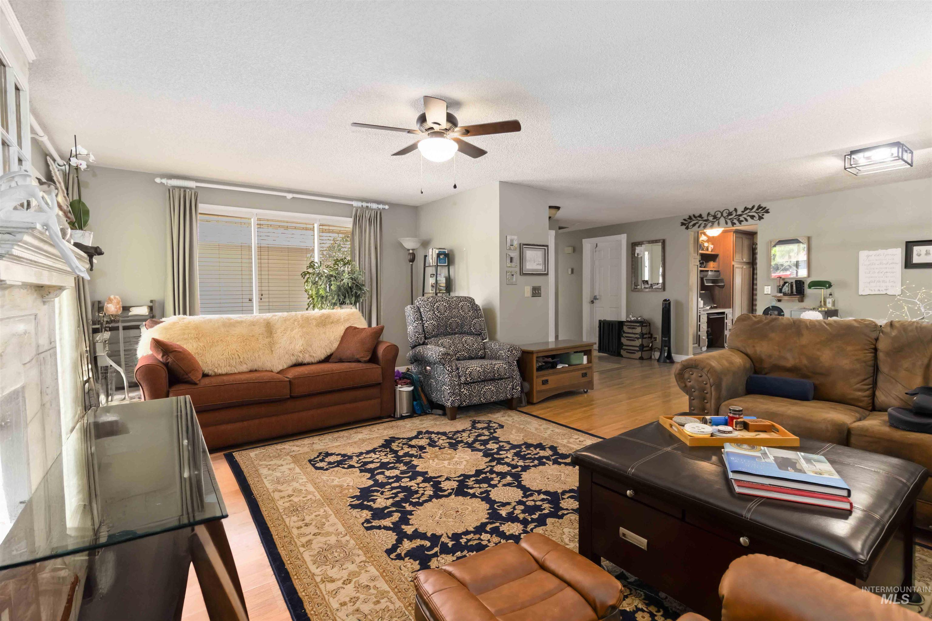 Living area with light wood finished floors, a premium fireplace, a ceiling fan, and a textured ceiling
